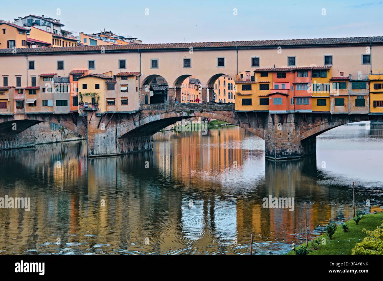 Florenz, Italien - Mai 2026: Historische Ponte-Vecchio-Brücke mit farbenfrohen Geschäften und Vasarigang, die sich im Arno spiegeln Stockfoto