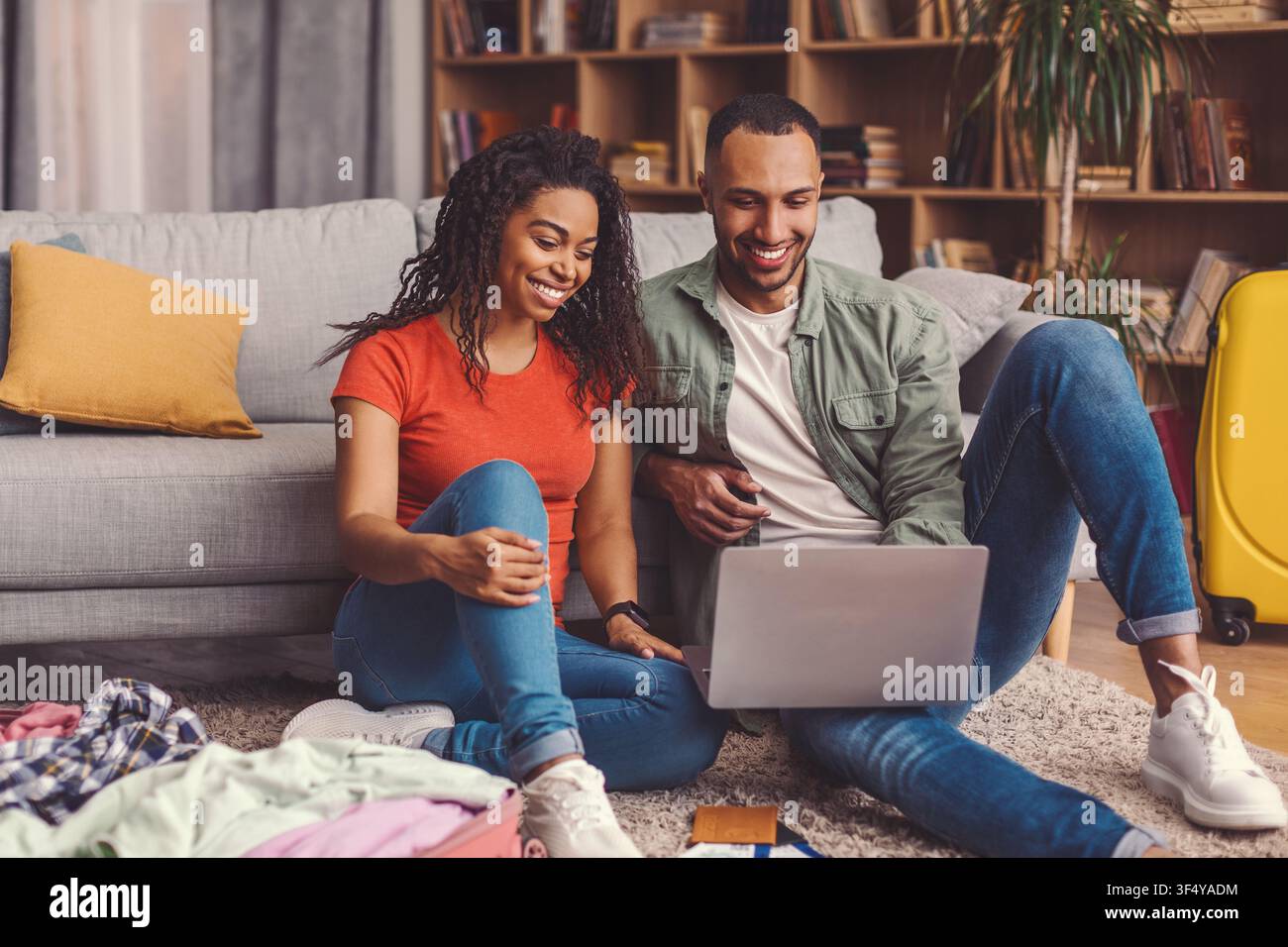 Glückliches junges multikulturelles Paar entspannt sich auf dem Sofa, während es zu Hause einen Laptop benutzt, Lebensstilkonzept Stockfoto