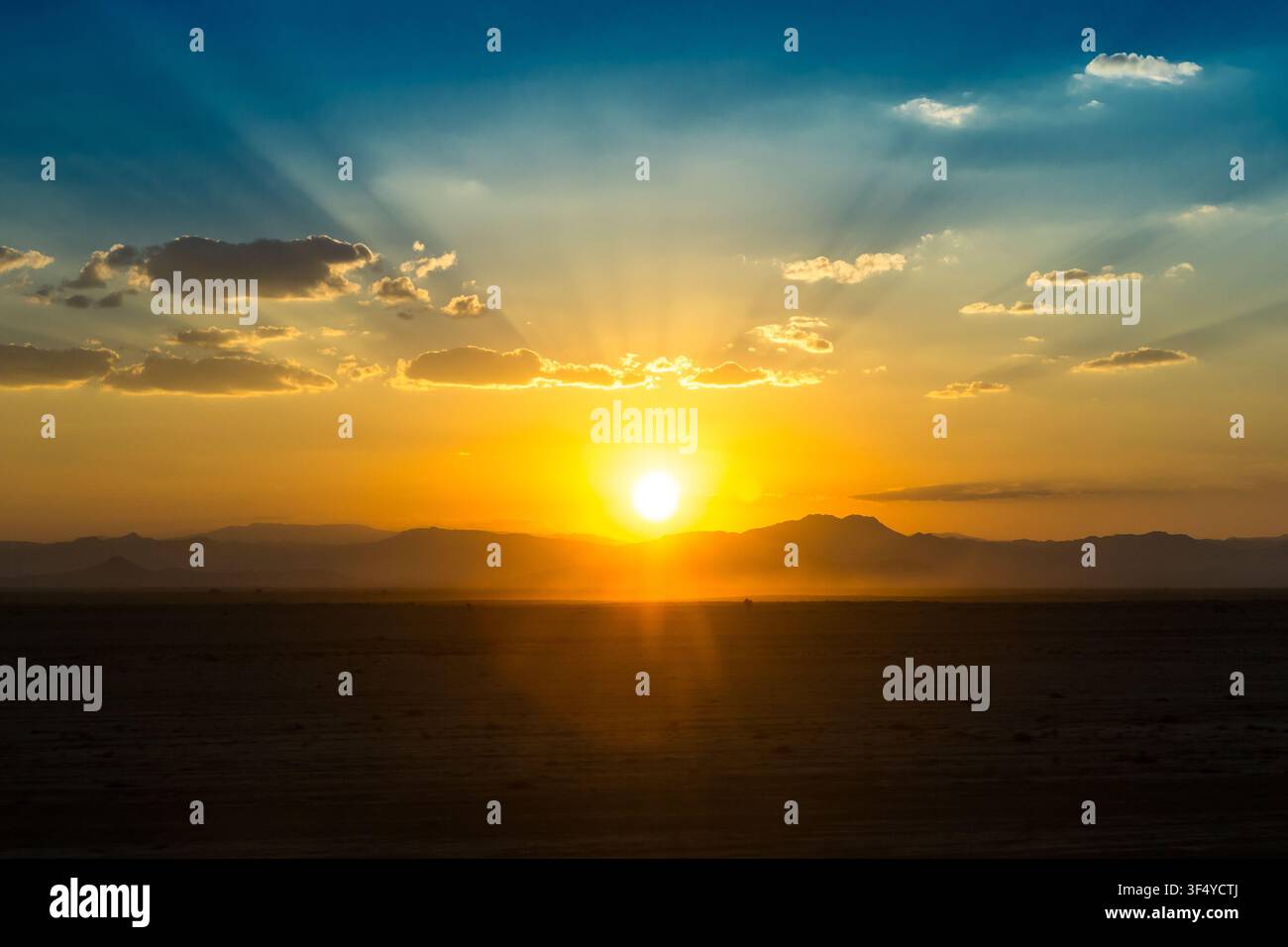 Blick auf die untergehende Sonne über der vulkanischen Landschaft von Erta Ale mit goldenen Strahlen, die den Horizont in Zone 2, Afar, Äthiopien beleuchten. Stockfoto