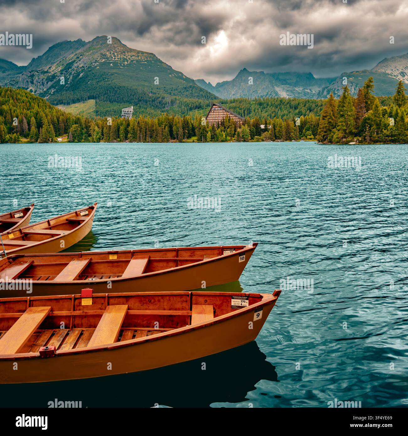 Traditionelle Holzruderboote auf dem Štrbské pleso See mit dramatischen Sturmwolken und den Hochtatra-Bergen im Hintergrund, Slowakei. Stockfoto