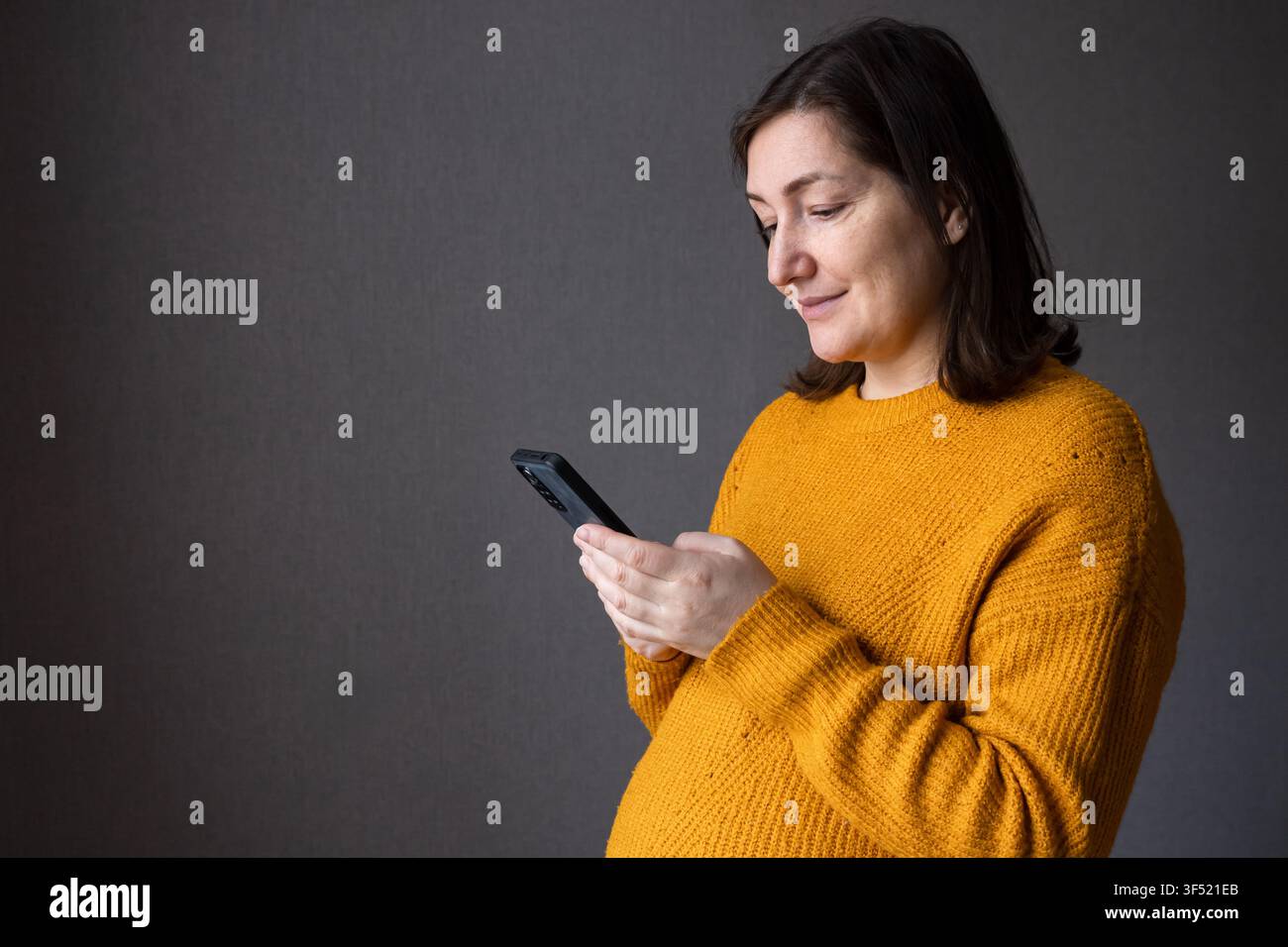 Schwangere Frau in gelbem Pullover, die ihren Bauch hält und ihn sanft mit den Händen berührt Stockfoto