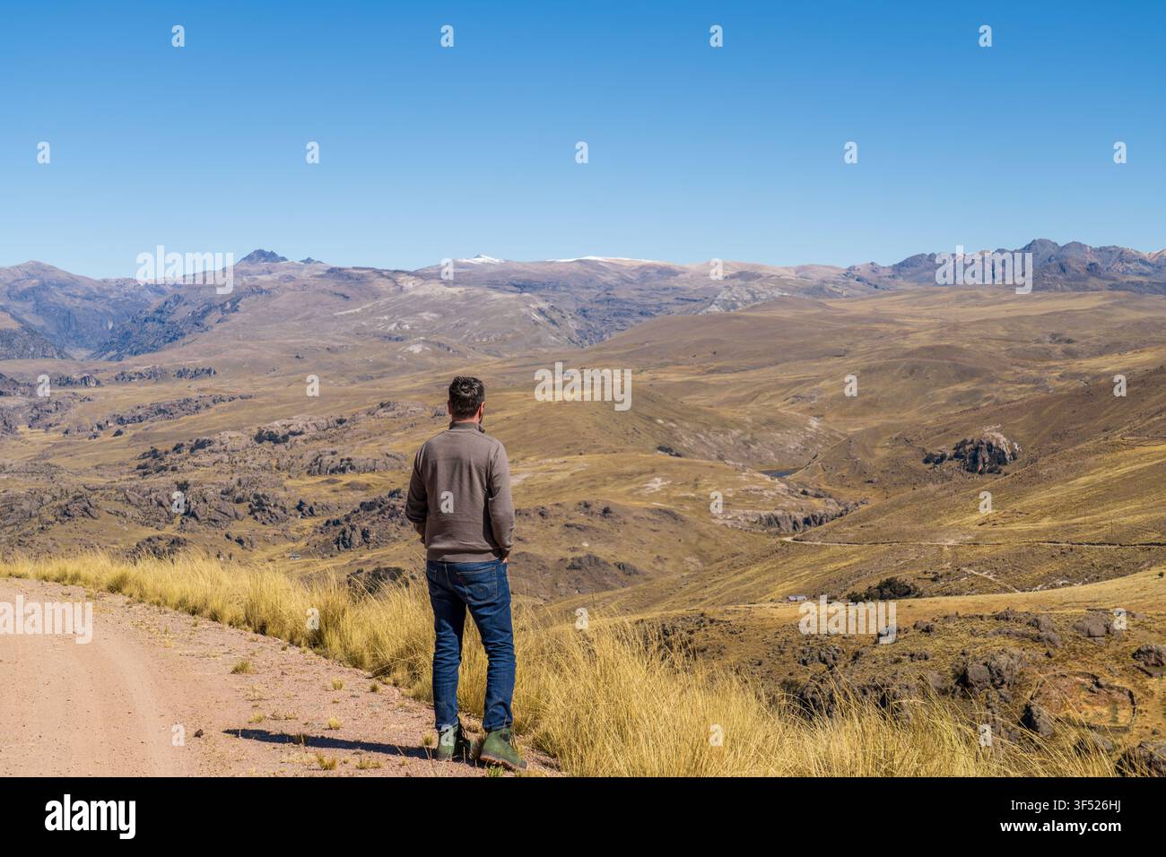 Rückansicht eines Mannes, der auf einer Schotterstraße steht und auf die weite und trockene Landschaft des peruanischen Altiplano unter einem klaren blauen Himmel blickt Stockfoto