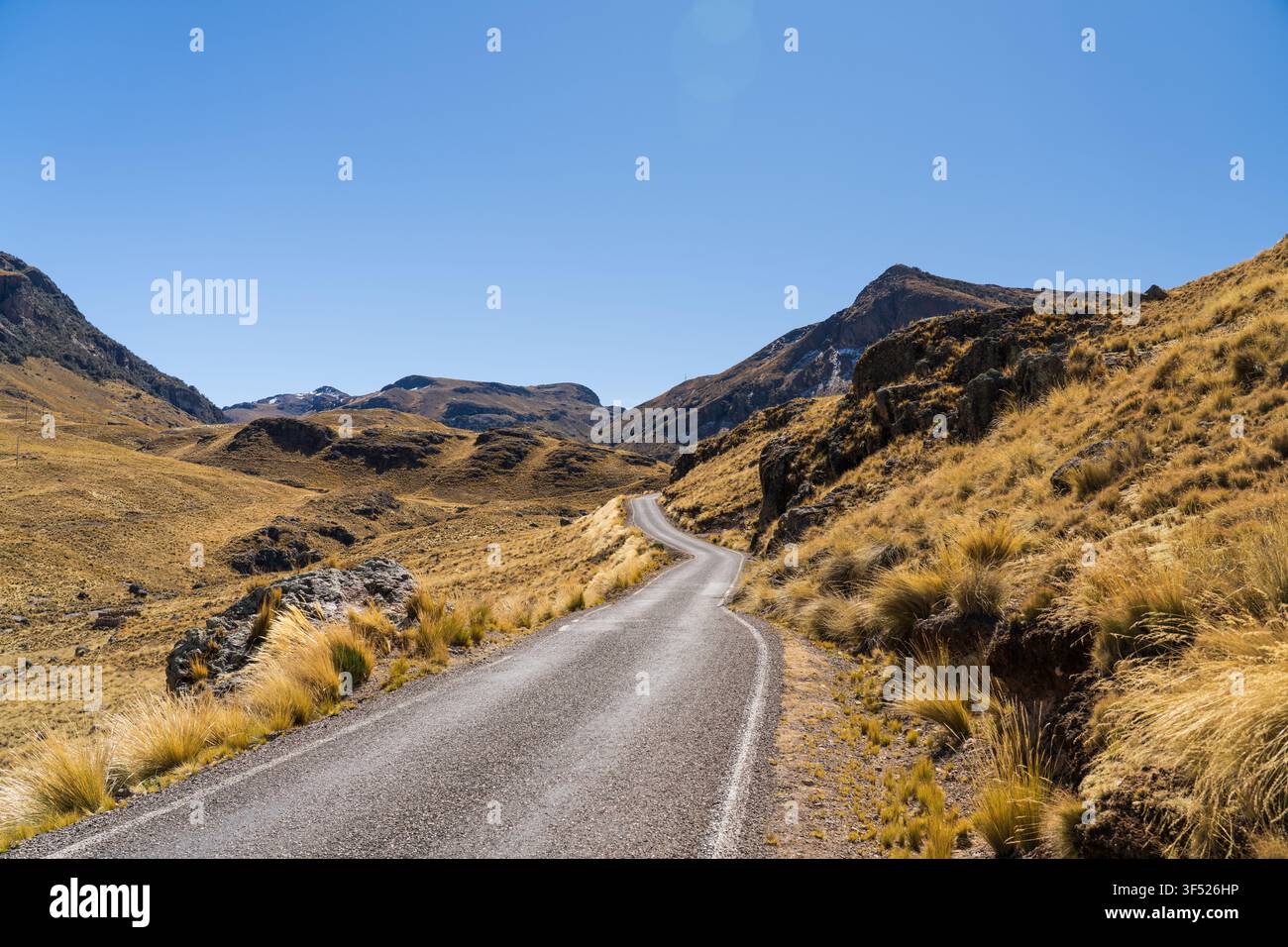 Eine sich windende gepflasterte Straße, die sich durch die weite und trockene Hochgebirgslandschaft des peruanischen Altiplano unter einem klaren blauen Himmel erstreckt Stockfoto