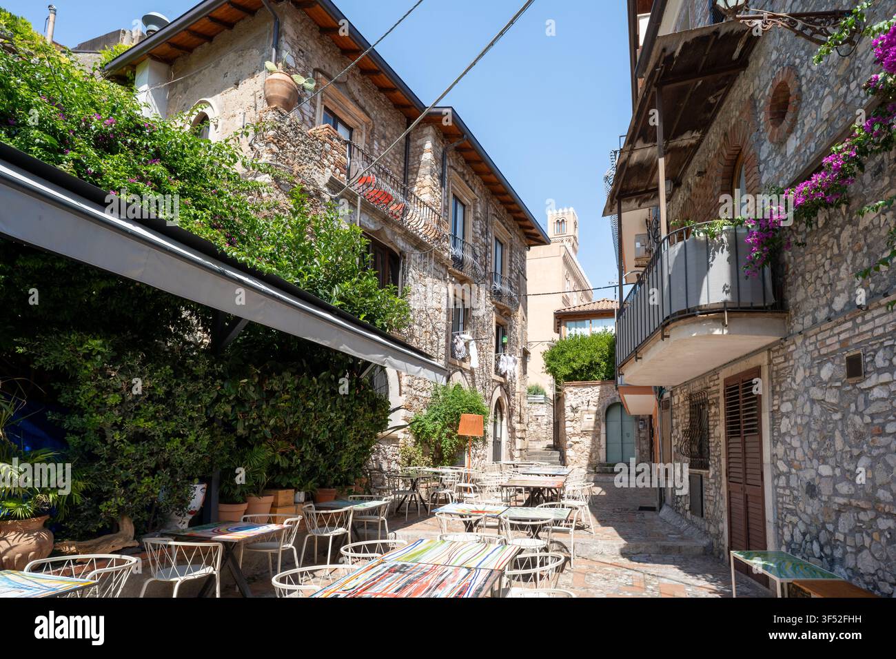 Leere Restauranttische für Speisen im Freien zwischen historischen Steinbauten in Taormina, Sizilien Stockfoto