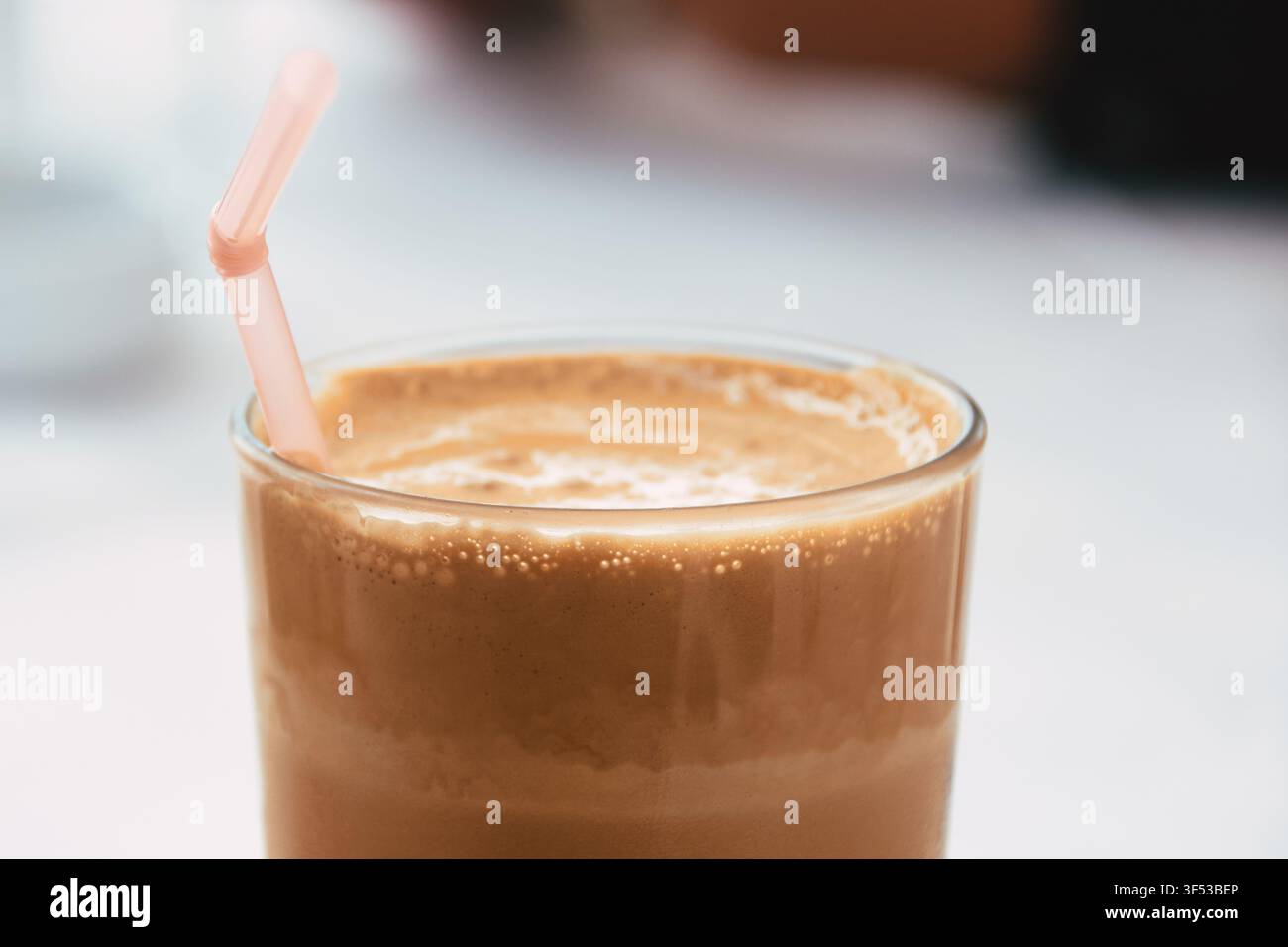 Eine Nahaufnahme eines kalten, schaumigen Eiskaffees, serviert in einem klaren Glas mit einem rosa Plastikstrohhalm, der aufrecht im köstlichen Getränk steht Stockfoto