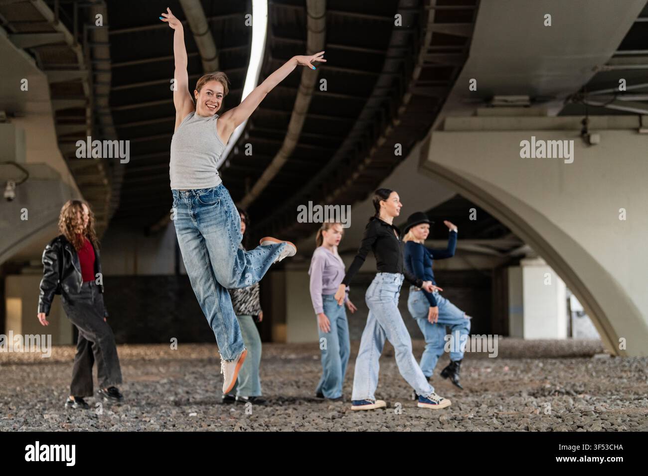 Fröhliche junge Frau springt mit Freunden unter einer Brücke Stockfoto