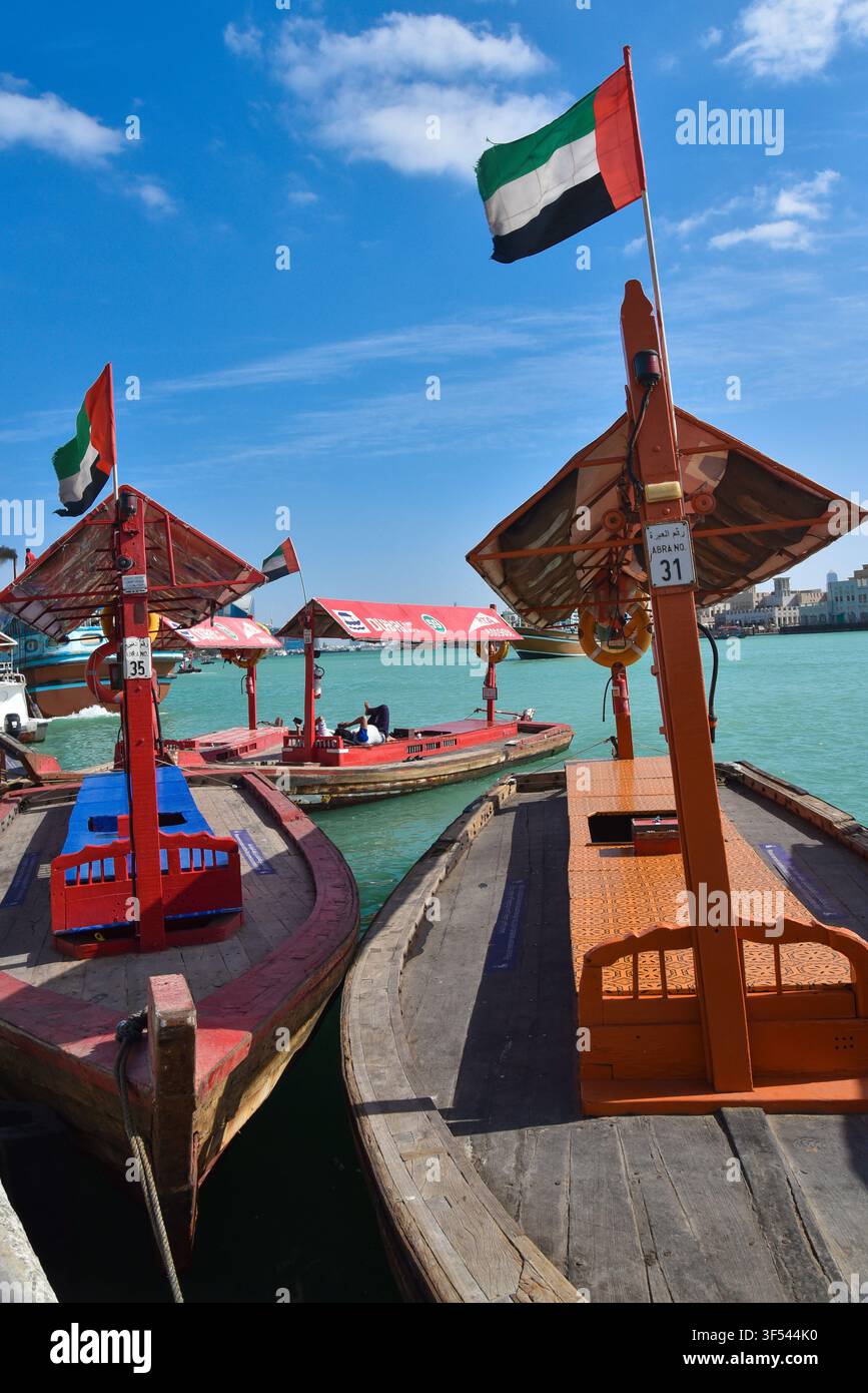 Traditionelle hölzerne Abra-Wassertaxis mit UAE-Flaggen, die entlang des türkisfarbenen Wassers des Dubai Creek in Bur Dubai, UAE, festgemacht sind. Stockfoto