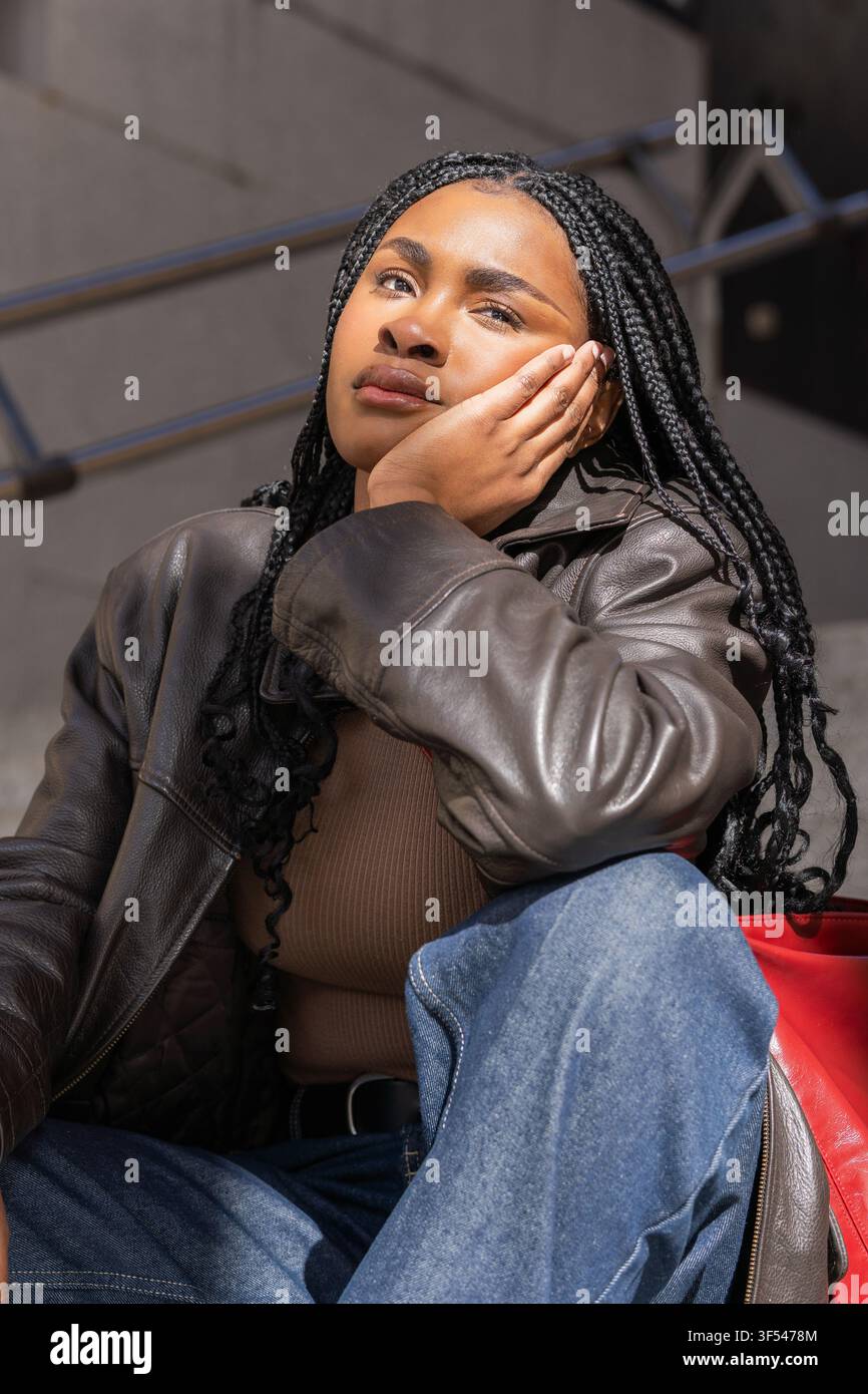 Nachdenkliche junge Frau, die das Kinn auf der Hand ruht, in Gedanken verloren, während sie draußen sitzt Stockfoto