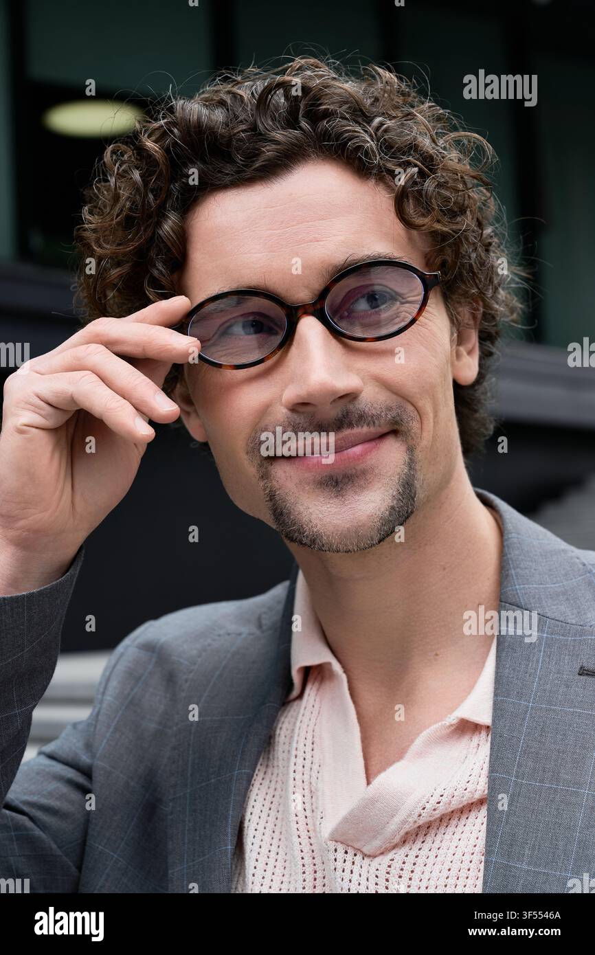 Lockenköpfiger Herr in eleganter Kleidung schreitet selbstbewusst durch eine geschäftige urbane Szenerie. Stockfoto