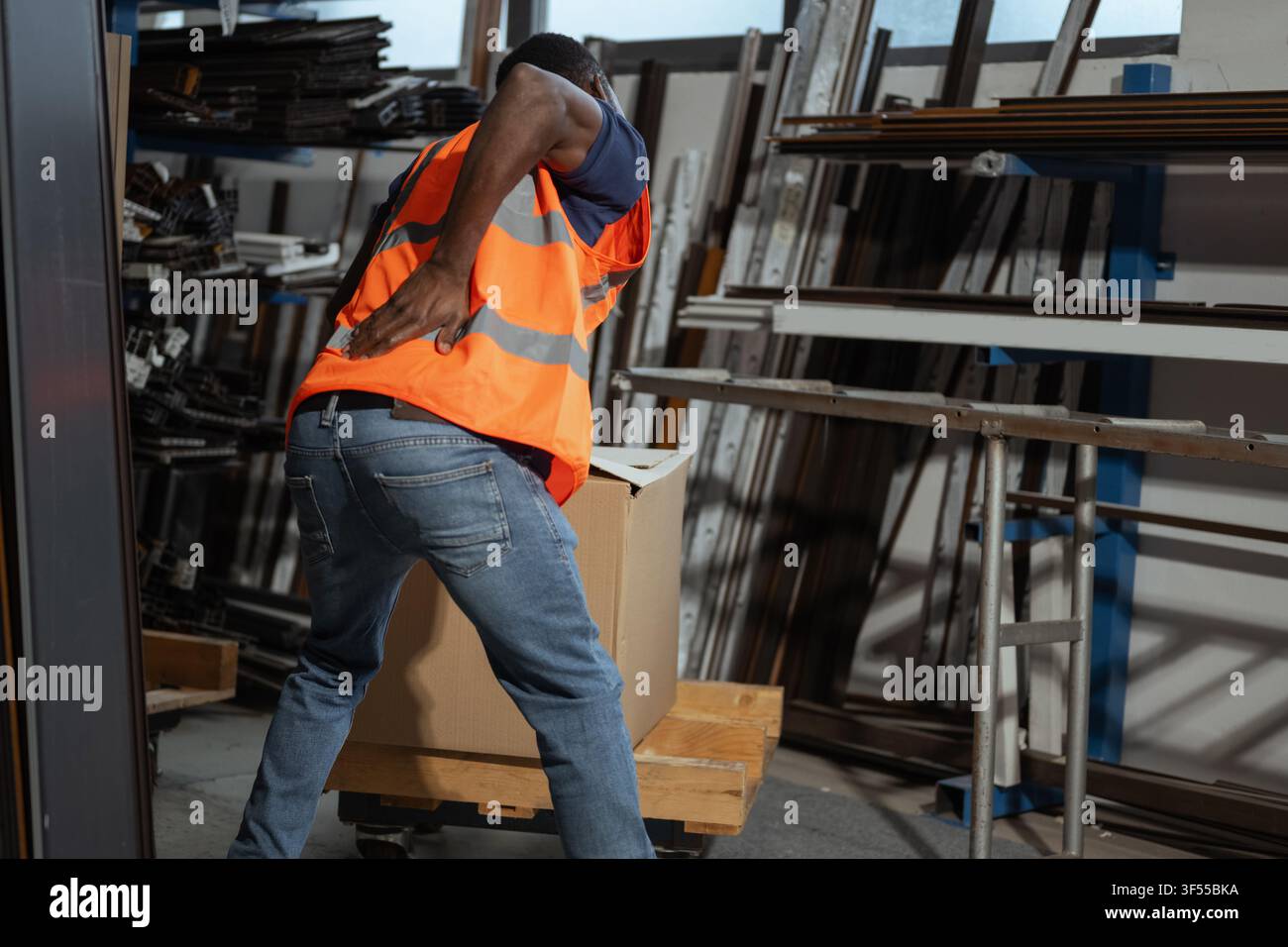 Arbeiter erlebt Schmerzen im unteren Rücken beim Heben einer schweren Kiste in einem Fabriklager während einer manuellen Aufgabe. Stockfoto