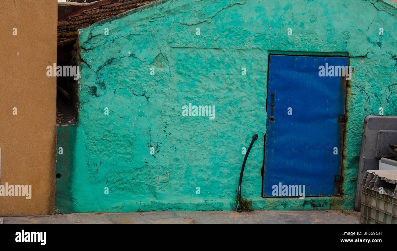 Blaue Metalltür in einer rissigen türkisfarbenen Wand eines Fischerhauses, Portugal Stockfoto