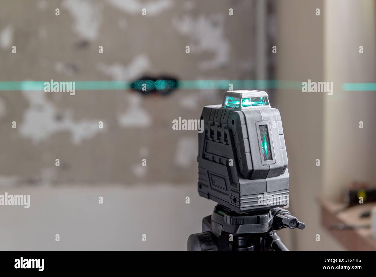 Ein auf einem Stativ montierter Laserniveauprojektor projiziert eine grüne Linie auf eine Bausteinwand. Ein Laserniveauprojektor ist unverzichtbar für präzise Ausrichtungen und Messungen. Stockfoto