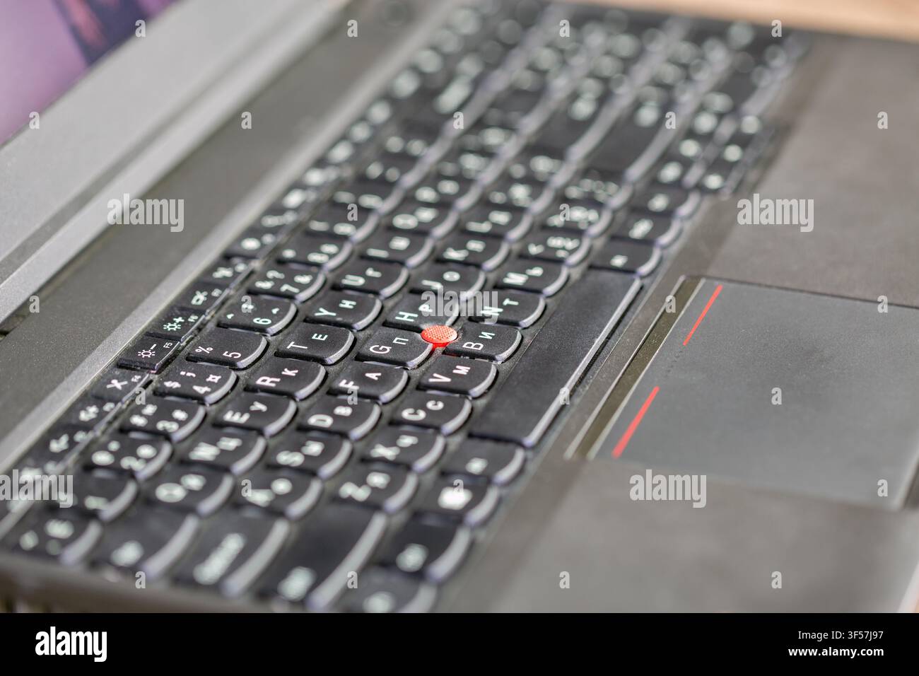 Makroaufnahme einer Laptop-Tastatur, die schwarze Tasten mit weißen Buchstaben und einen markanten roten Trackpoint-Knopf zeigt. Professionelles Computerkonzept. Technik Stockfoto