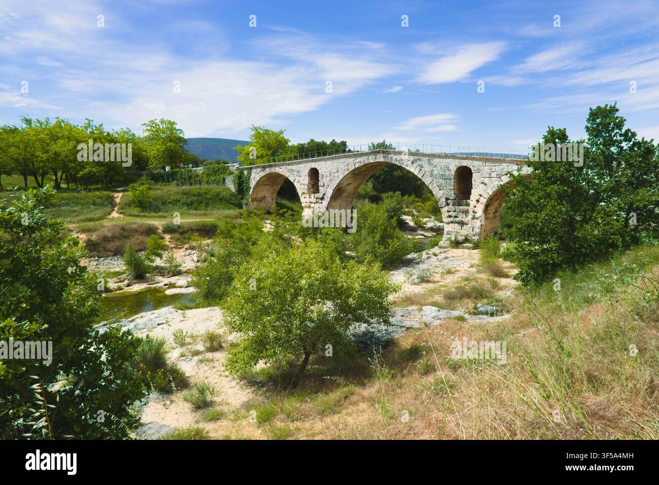 Die antike römische Steinbogenbrücke Pont Julien, eingerahmt von grünen Bäumen und Feldern in Bonnieux, Provence, Frankreich. Stockfoto