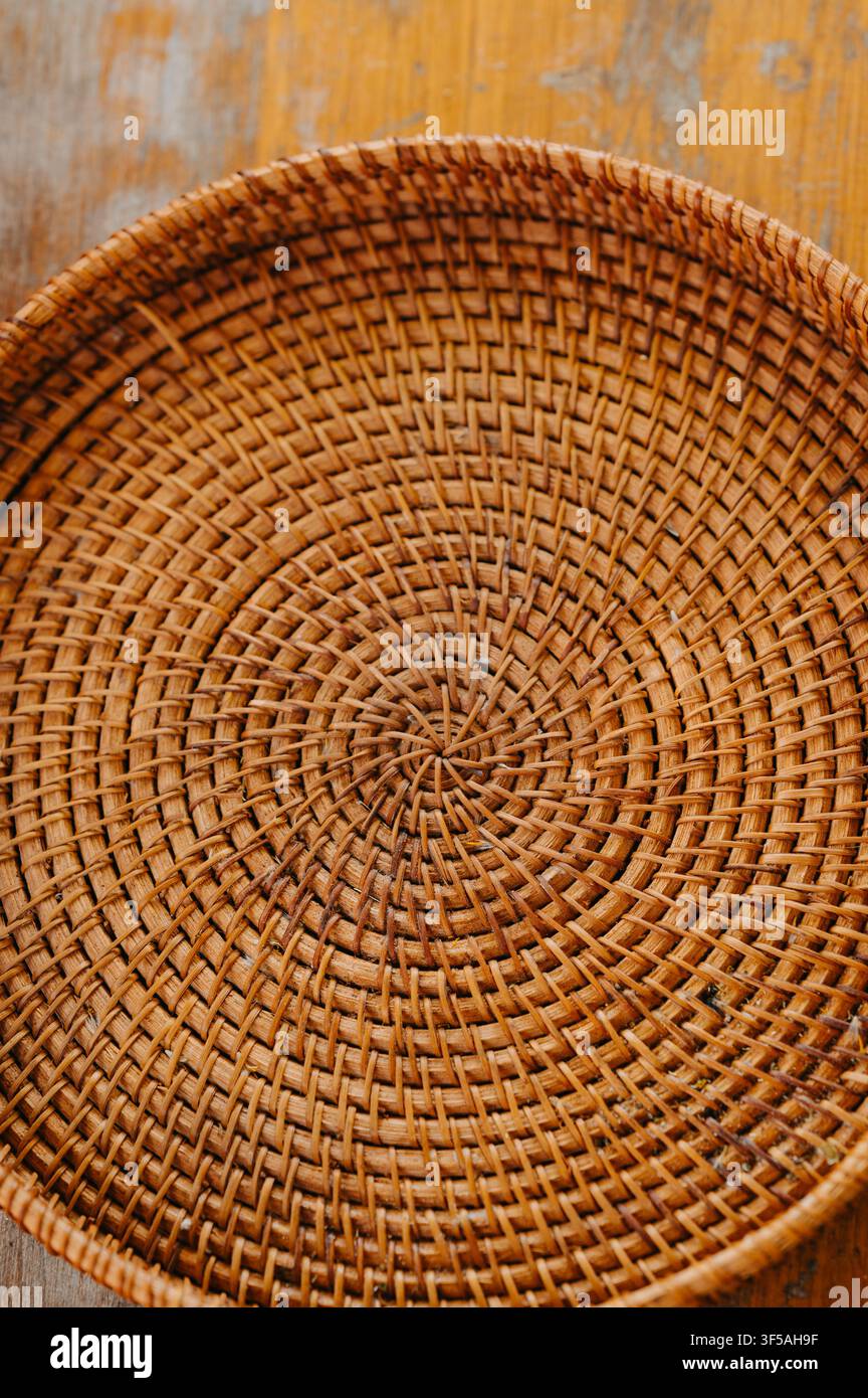Runder geflochtener Rattan-Korb mit spiralförmiger Textur, der auf einer Holzoberfläche ruht und natürliche braune Fasern zeigt, handwerklich hergestellt Stockfoto