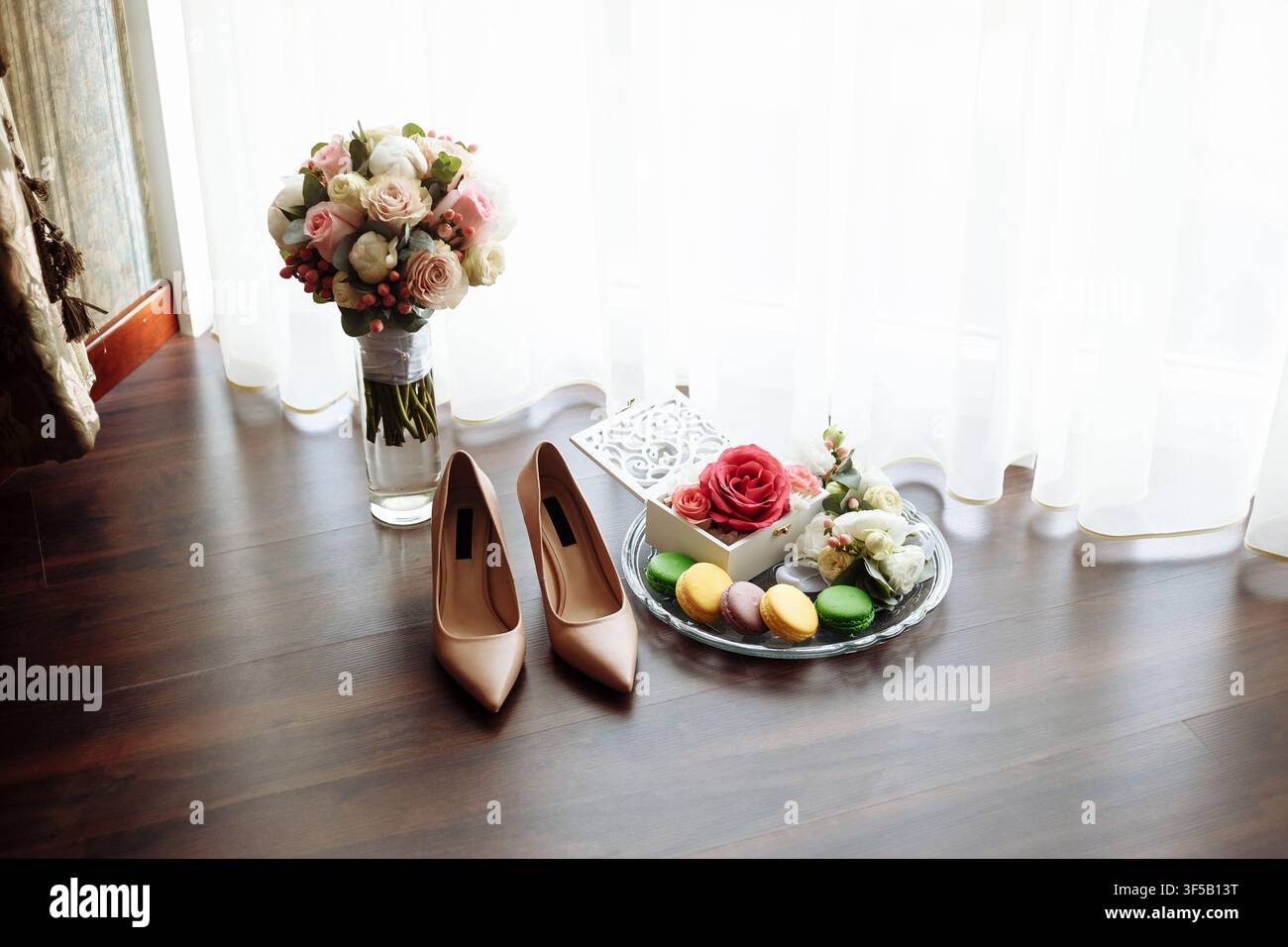 Elegante Hochzeitsaccessoires mit bunten Macarons und einem Brautstrauß auf einem Holzboden. Konzept von Hochzeitsdetails, Brautvorbereitung, Flat-Lay-Styling und romantischer Feier Stockfoto