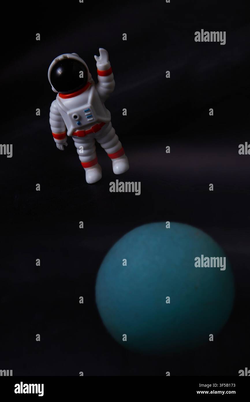 Ein Miniatur-Astronaut scheint durch den tiefen Weltraum über einem leuchtend blauen Planeten zu schweben und erzeugt eine verspielte und phantasievolle Szene Stockfoto