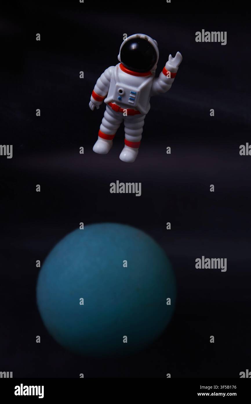 Ein Miniatur-Astronaut scheint im Weltraum zu schweben und winkt über einem leuchtend blauen Planeten Stockfoto