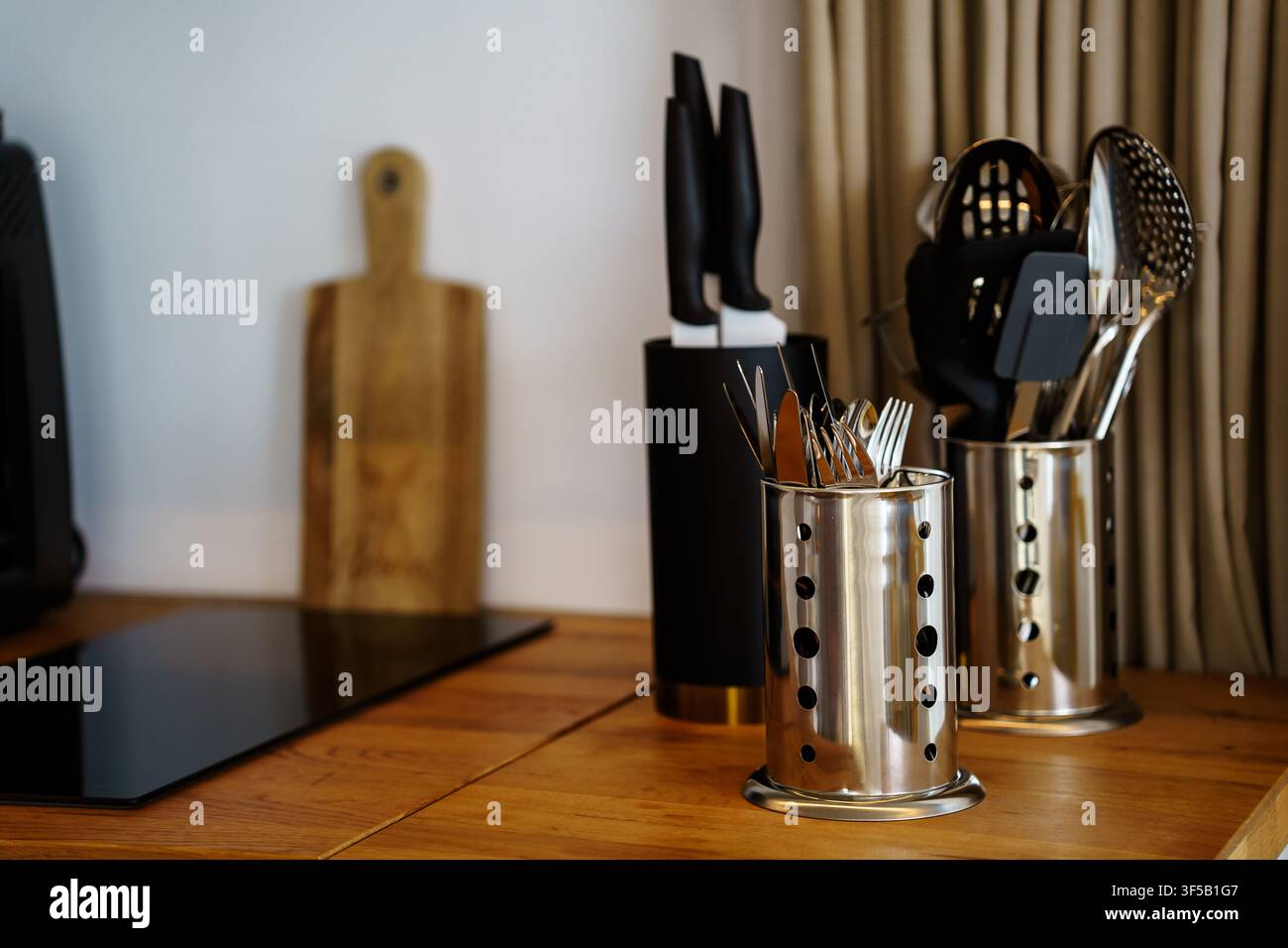 Moderne Küchenarbeitsplatte mit Edelstahl-Geschirrhaltern und einem Messerblock auf einer Holzoberfläche. Konzept für minimalistisches Küchendesign, Kochutensilien, Organisation und Mahlzeitvorbereitung Stockfoto