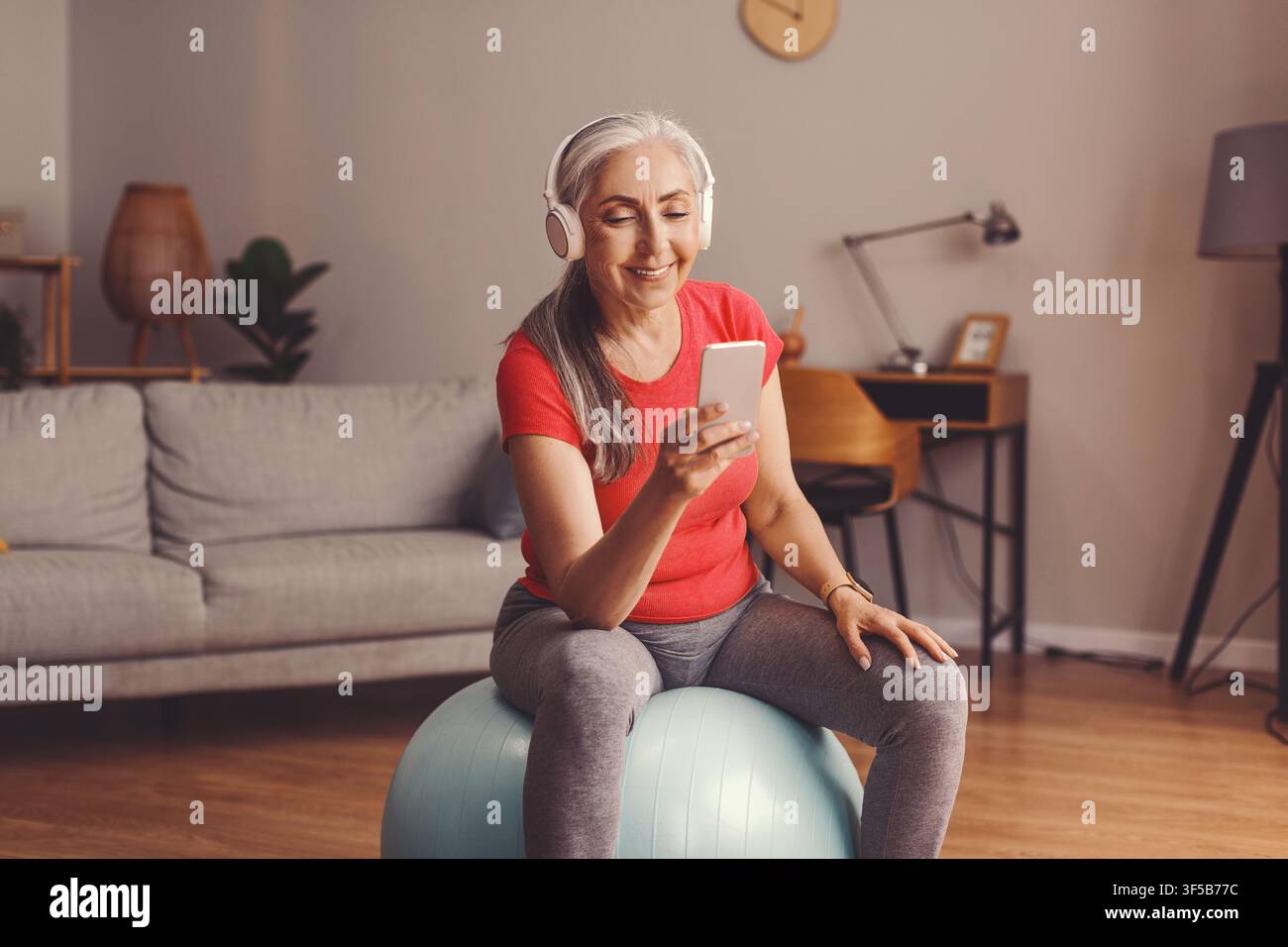 Zufriedene ältere kaukasische Frau hört Musik, während sie zu Hause ihr Smartphone benutzt, Gewichtsabnahme-Konzept Stockfoto