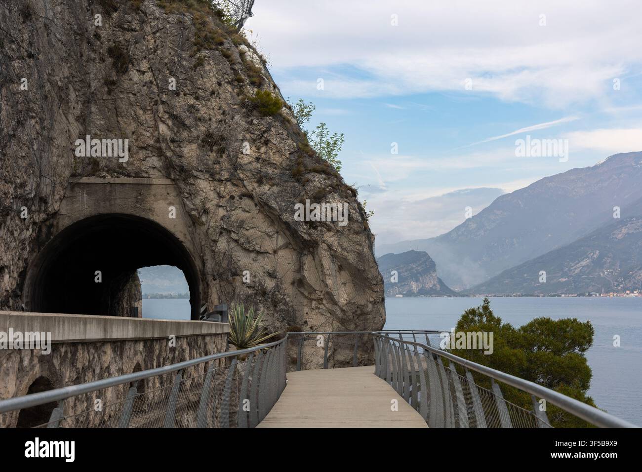 Fuß- und Radweg an der Klippenküste, der an einem Tunnel entlang des Gardasees mit Panoramablick auf die Berge in der Nähe von Limone sul Garda, Italien, führt. Stockfoto