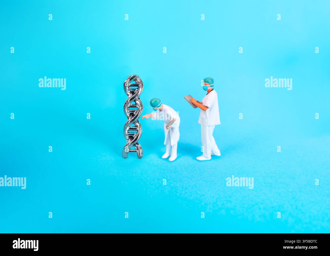 Miniaturfiguren von Wissenschaftlern in medizinischen Kittel, die ein metallisches DNA-Doppelstrangmodell untersuchen, symbolisieren genetische Forschung, Biotechnologie und Wissenschaft Stockfoto