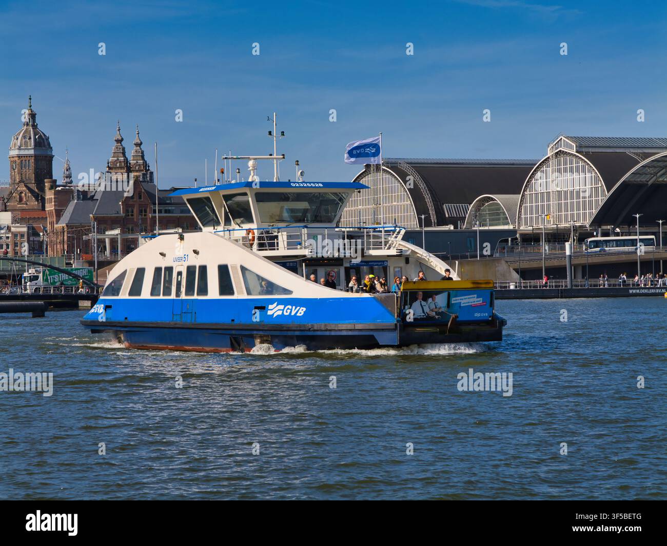 Amsterdam, Niederlande – 16. Apr 2026: Eine GVB-Passagierfähre überquert das IJ neben dem Amsterdam Centraal in den Niederlanden unter einem strahlend blauen Frühlingshimmel Stockfoto