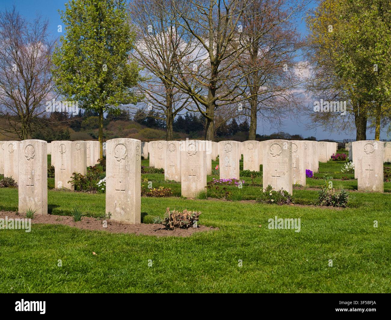 Groesbeek, Niederlande - 14. Apr 2026: Reihen weißer Militärgrabsteine zwischen grünen Rasenflächen und Frühlingsbäumen auf dem kanadischen Kriegsfriedhof Groesbeek, Niederlande Stockfoto