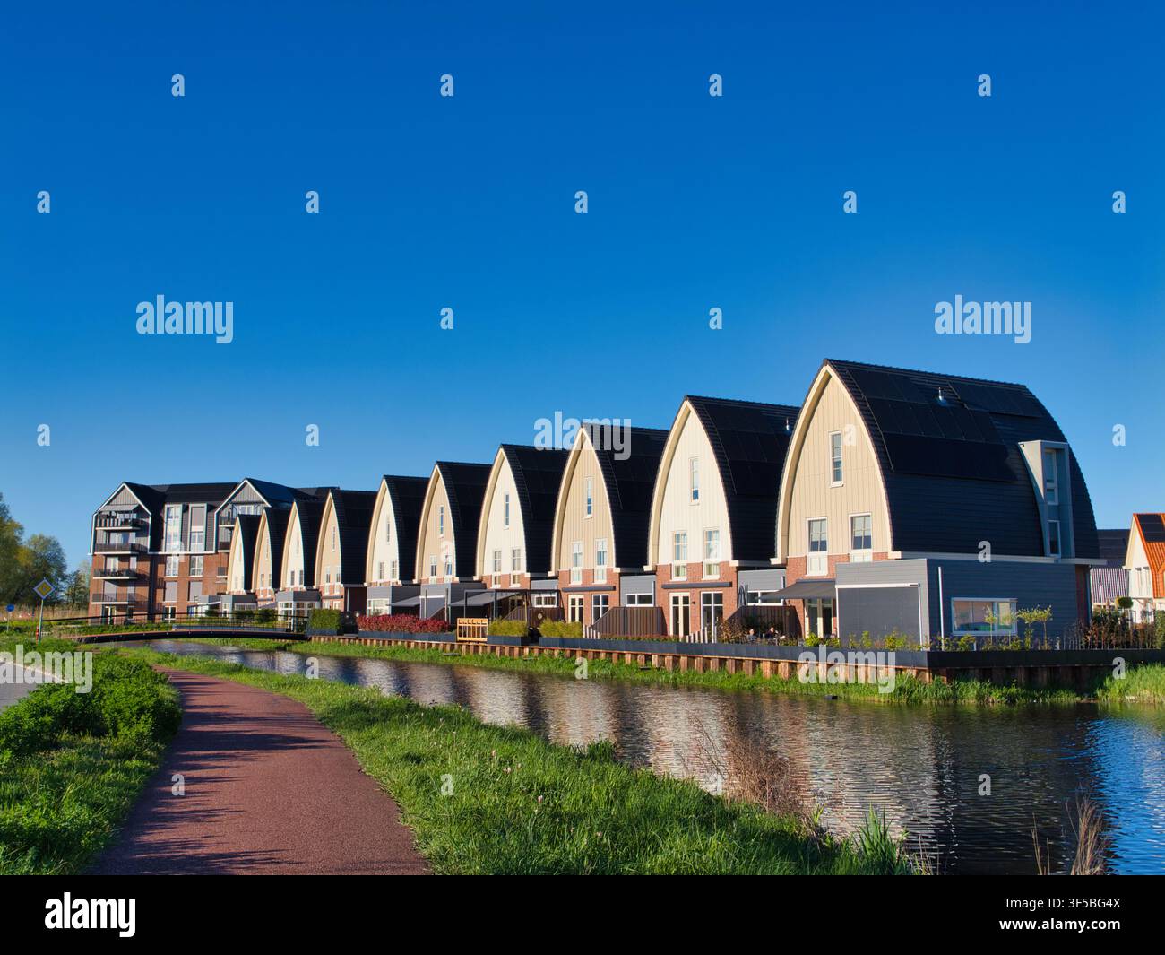 Niederlande - 18. Apr 2026: Moderne gewölbte Häuser neben einem Kanal in den Niederlanden unter einem klaren blauen Abendhimmel Stockfoto