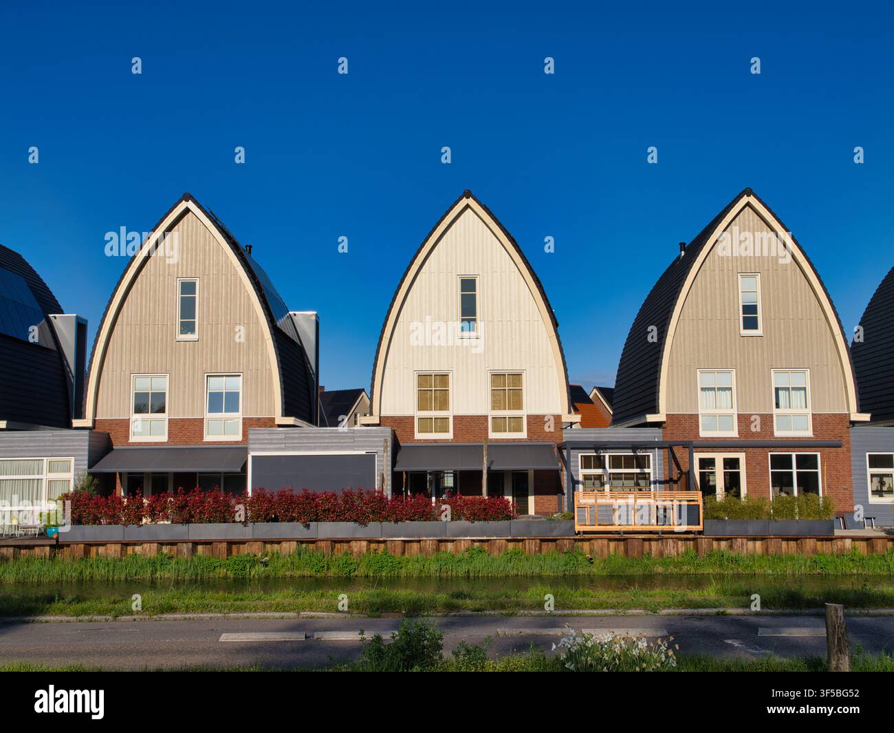 Niederlande - 18. Apr 2026: Zeitgenössische gewölbte Häuser entlang einer Uferstraße in den Niederlanden leuchten im warmen Abendlicht unter einem klaren blauen Himmel Stockfoto