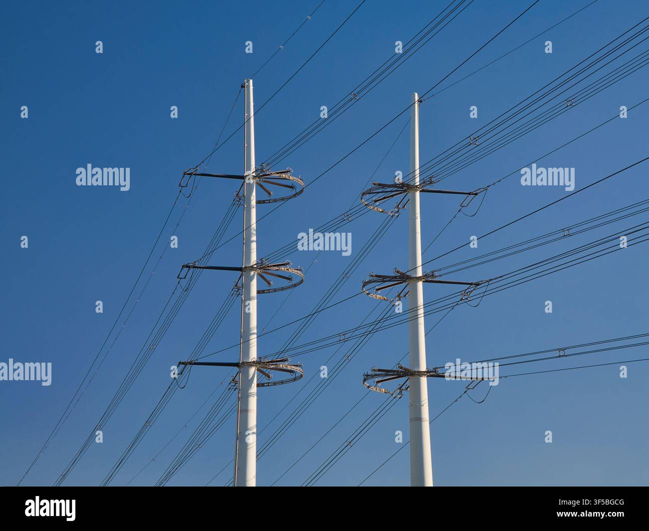 Niederlande – 21. Apr 2026: Hohe Strommasten und Stromleitungen bilden kühne geometrische Muster vor einem klaren blauen Himmel in den Niederlanden Stockfoto