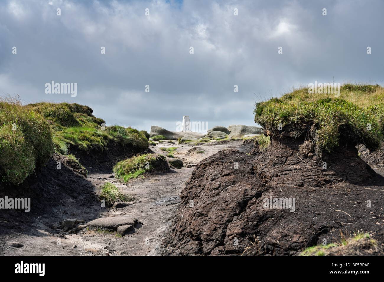 Der weiße Beton-Dreipunktpfeiler auf dem Gipfel von Bleaklow Head steht eingerahmt von dunklen, tief erodierten Torfmooren unter einem bewölkten Himmel im Peak District Stockfoto