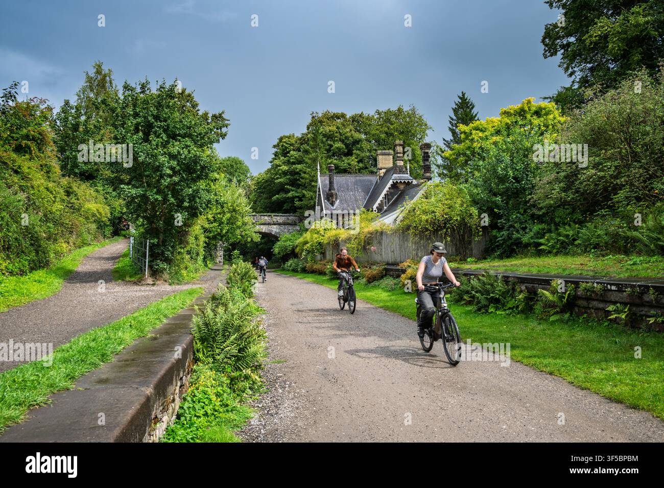 Radfahrer fahren den Schotterweg des Monsal Trail entlang, vorbei an der wunderschön erhaltenen Steinplattform und den Gebäuden des Bahnhofs Great Longstone Stockfoto