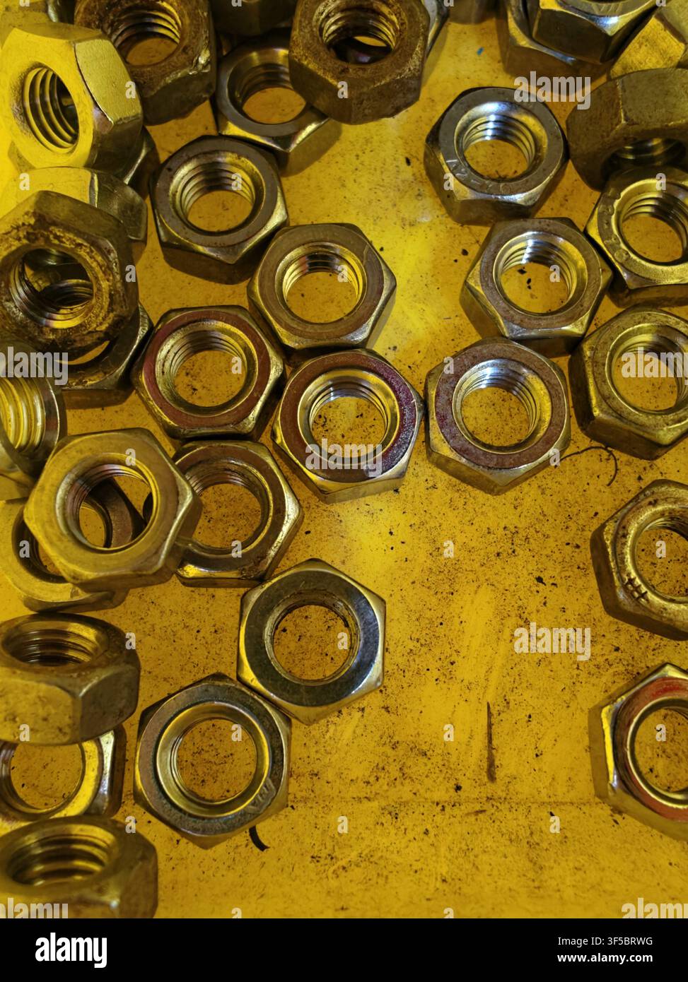 Nahaufnahme von verschiedenen Sechskantmuttern und Gewindebolzen, die über eine gelbe Metallarbeitsfläche verstreut sind und eine starke Textur, Farbkontrast und Praktikabilität erzeugen Stockfoto