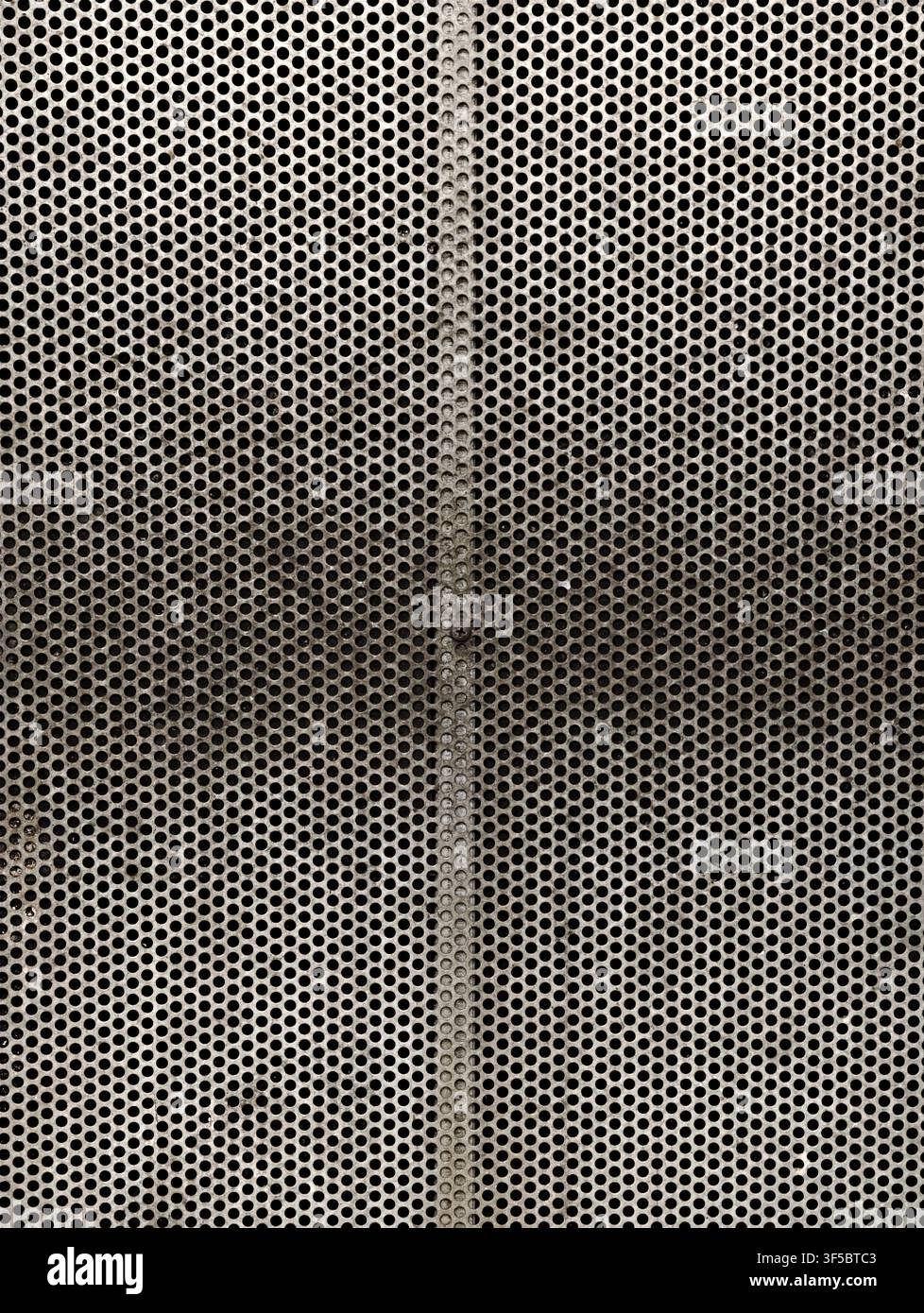 Nahaufnahme einer perforierten Metallplatte mit gleichmäßigen runden Öffnungen, zentraler vertikaler Naht, subtilen Reflexionen und sich wiederholender industrieller Textur ac Stockfoto