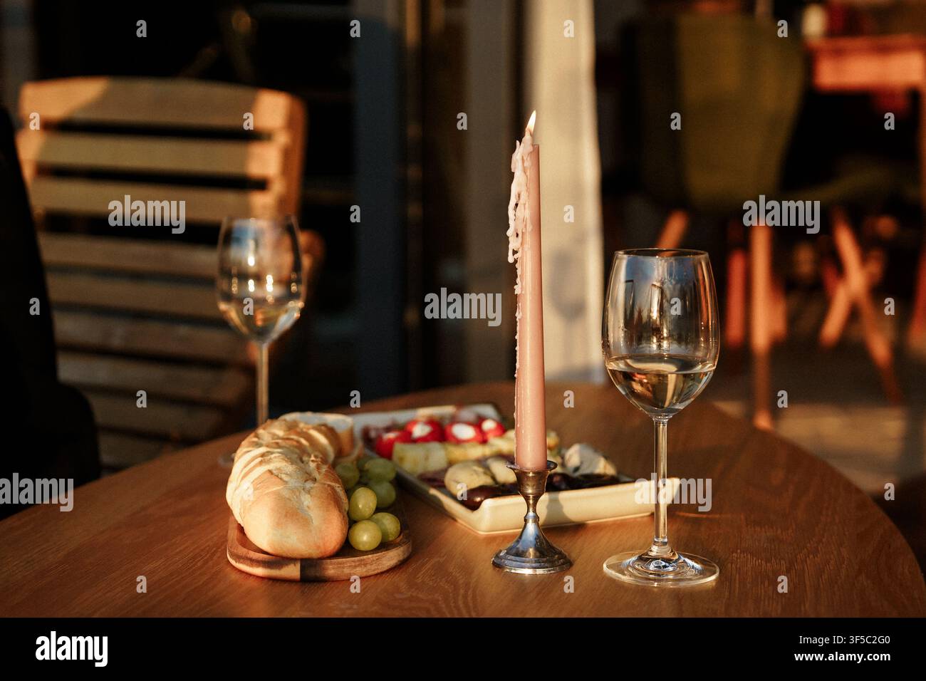Romantisches Abendessen-Tisch-Setup mit Weingläsern, Kerzenlicht und frischem Brot auf einem Holztisch bei Sonnenuntergang. Intime Golden-Hour-Date-Nacht, rustikales Outdoor-Esserlebnis Stockfoto