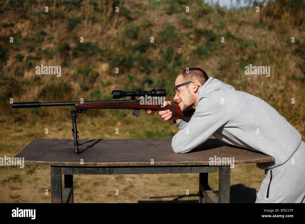 Konzentrierter Mann schießt mit Präzisionsgewehr mit Zielfernrohr auf einem Schießstand im Freien an einem sonnigen Tag. Professionelles Schießtraining, Langstreckenzielschießen als Hobby, Feuerschutzsport, Outdoor-Hobby Stockfoto
