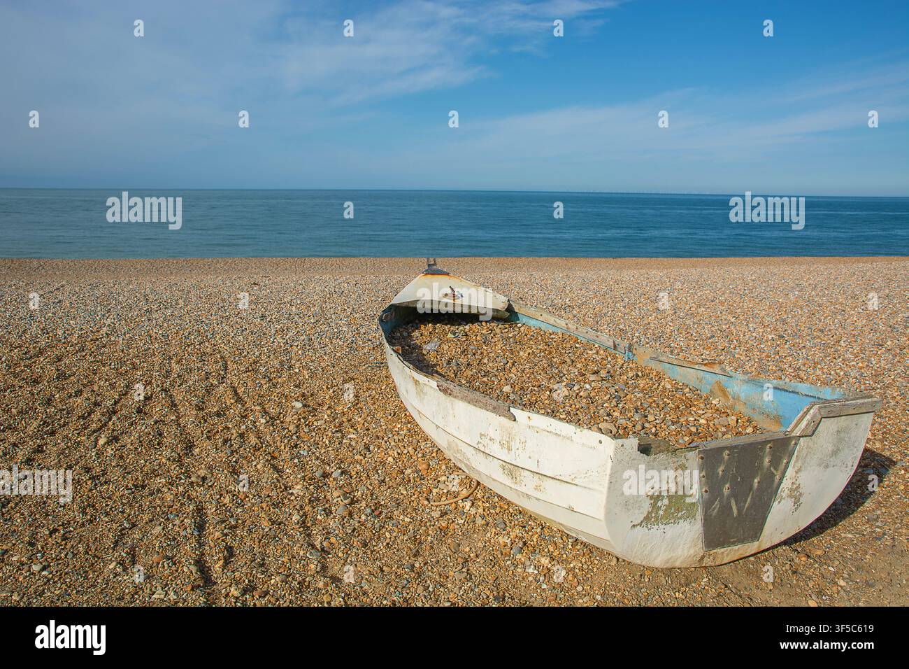 Verlassenes Fischerboot, gefüllt mit Strandkies, gestrandet am Strand von Seaford Stockfoto