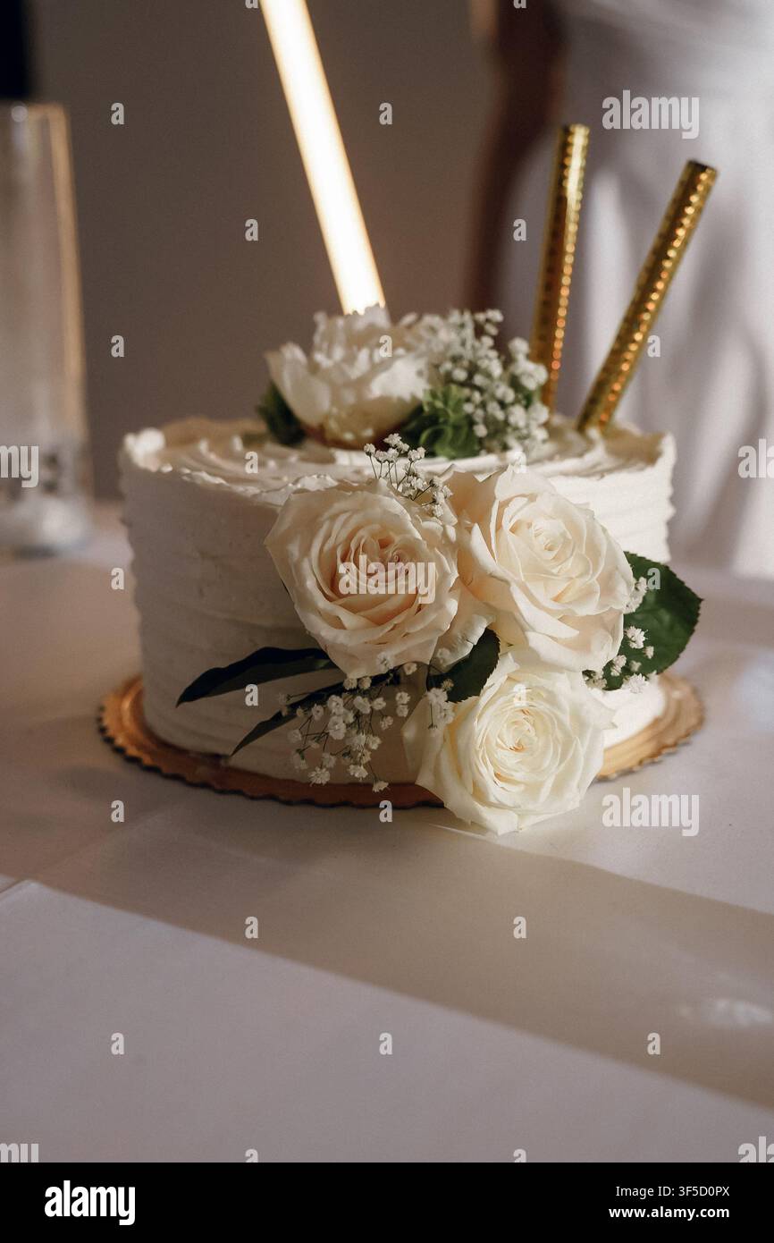 Ein eleganter weißer Hochzeitstorte dekoriert mit frischen Sahnerosen und goldenen Glitzern. Luxus-Hochzeitsfeier, festliches Partydessert, anspruchsvolles Brautbankett und romantische Feierevent Stockfoto
