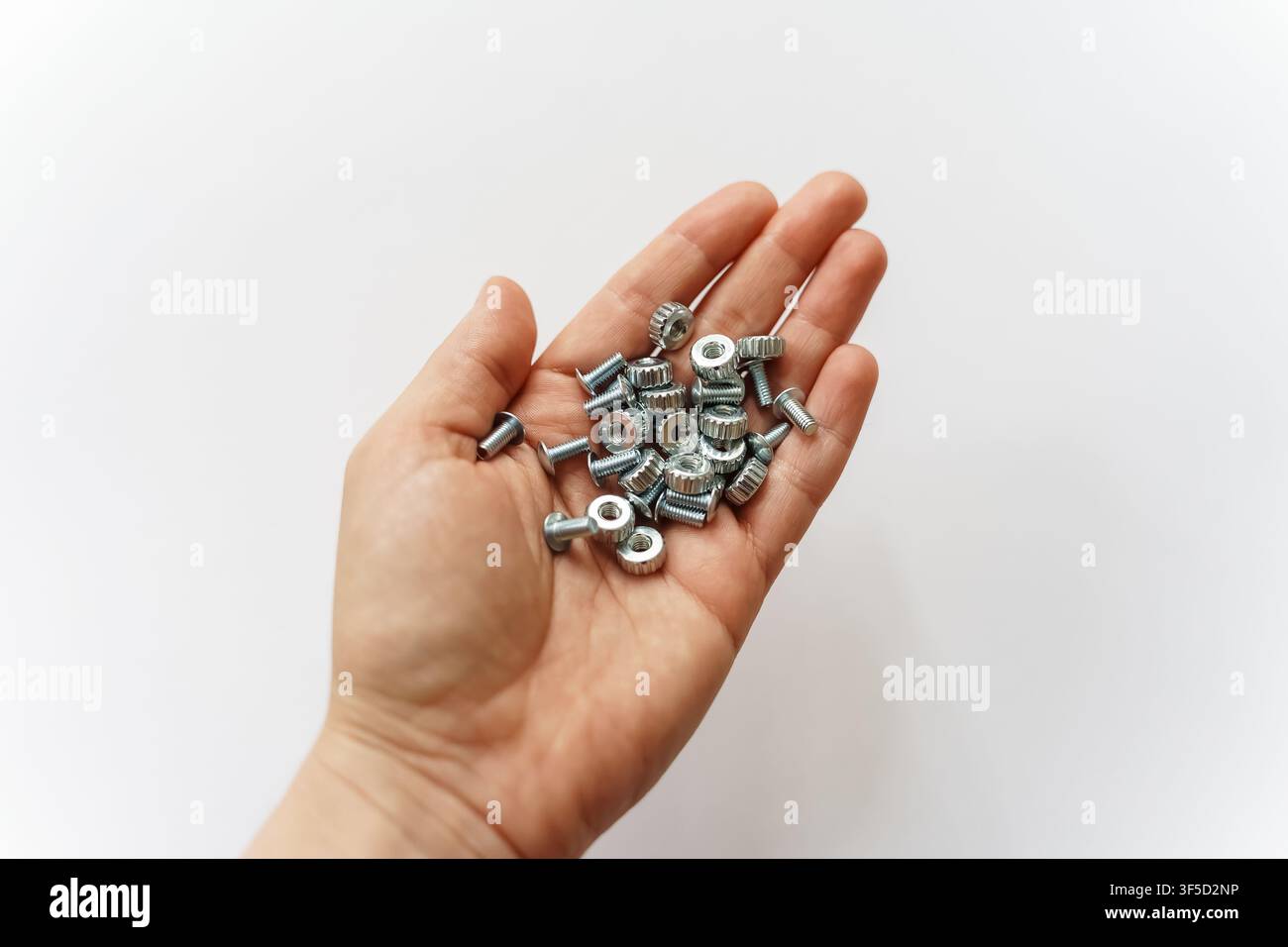 Eine offene menschliche Hand hält eine kleine Ansammlung von silbernen Metallmuttern und Schrauben, die Bau, Reparaturen, Heimwerkerarbeiten und industrielle Wartung darstellen Stockfoto