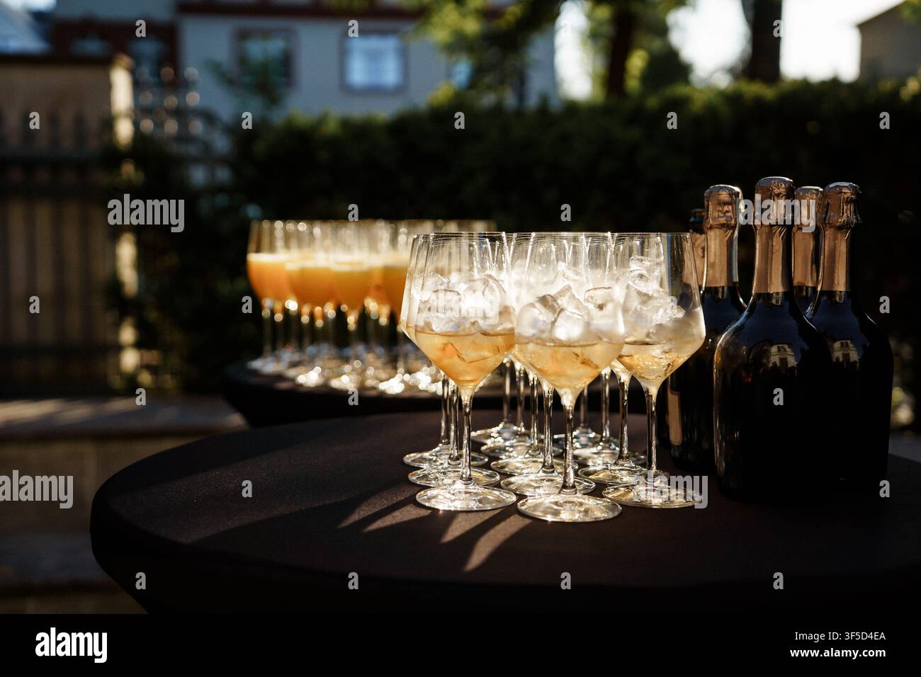 Sektgläser und Weinflaschen auf einem dunklen Außentisch bei Sonnenuntergang, die eine elegante Atmosphäre für Feiern, Hochzeiten und formelle Veranstaltungen einfangen, Festgetränke, eleganter Abend, Catering Stockfoto