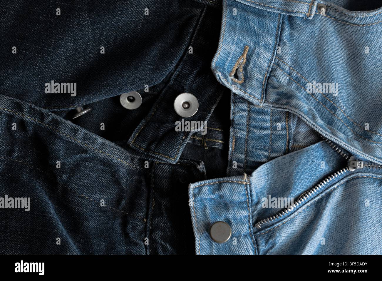 Nahaufnahme, die kontrastierende dunkle und helle Denimtexturen mit Metallknöpfen und einem Reißverschluss zeigt Stockfoto