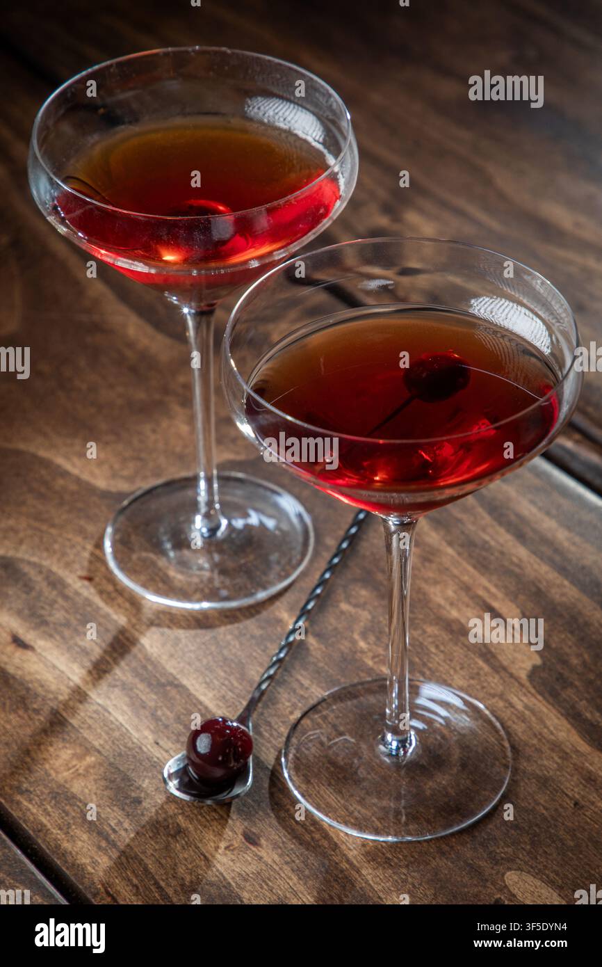 Zwei Whiskey-Manhattans serviert mit einer Kirsche auf einem rustikalen Holzgrund Stockfoto
