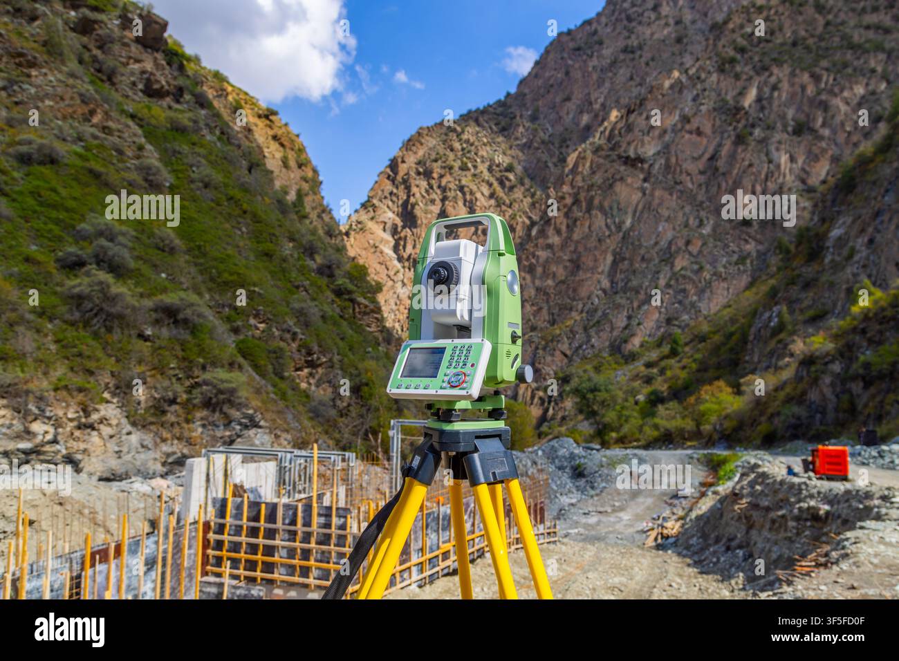 Digitales Totalstation-Vermessungsinstrument auf Stativ in einer rauen bergigen Landschaft in Kirgisistan. Baustelle zeigt hölzerne Schalung und Stockfoto