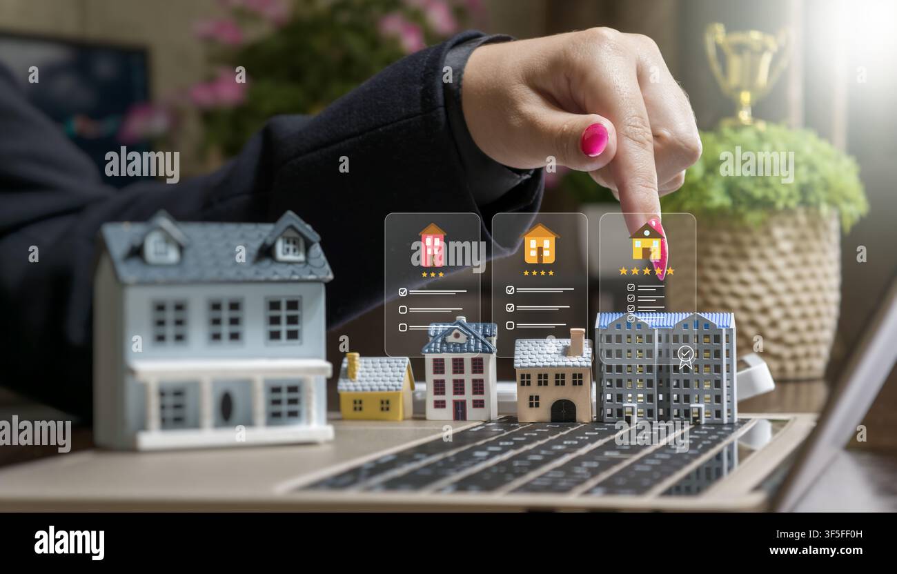 Kauf von Immobilien online: Frau wählt ein Miniaturmodellhaus auf einem Laptop mit virtuellen Smart-Home- und Hypotheken-Symbolen. Stockfoto