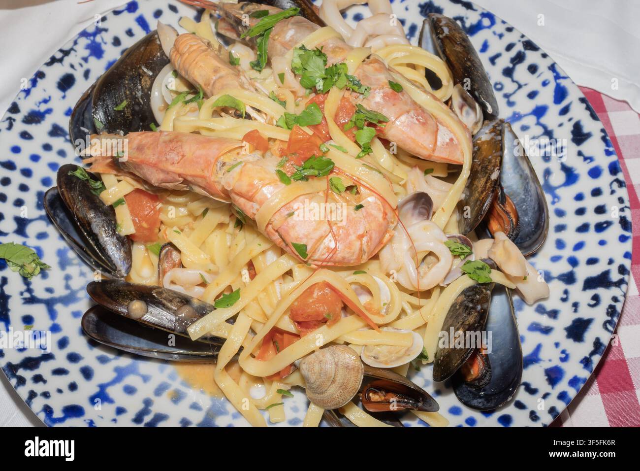 Authentische italienische Meeresfrüchte-Pasta mit Garnelen, Muscheln, Tintenfischen, Muscheln, Tomaten und frischen Kräutern, serviert auf einem Keramikteller in einem Restaurant. Stockfoto