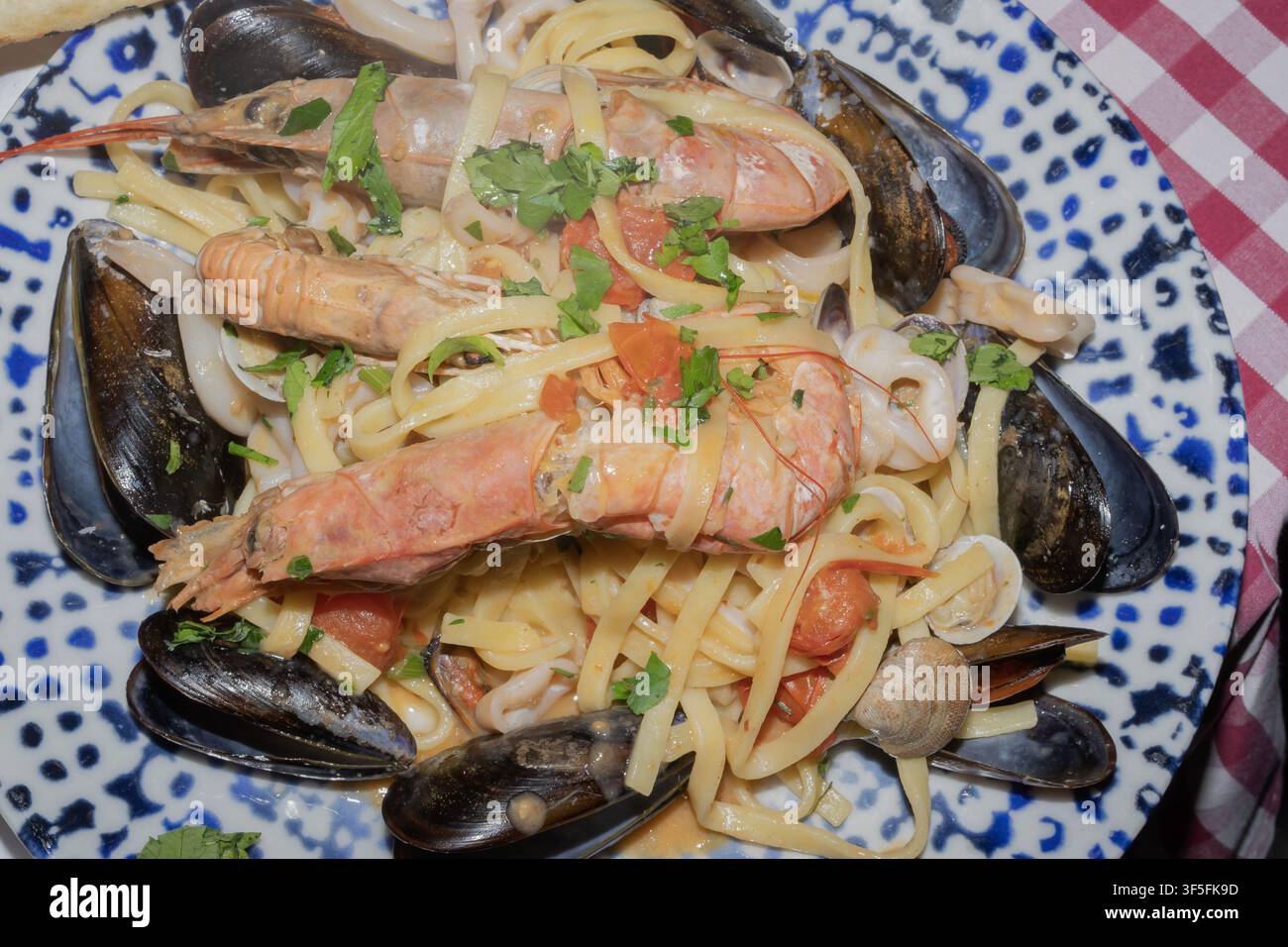 Authentische italienische Meeresfrüchte-Pasta mit Garnelen, Muscheln, Tintenfischen, Muscheln, Tomaten und frischen Kräutern, serviert auf einem Keramikteller in einem Restaurant. Stockfoto