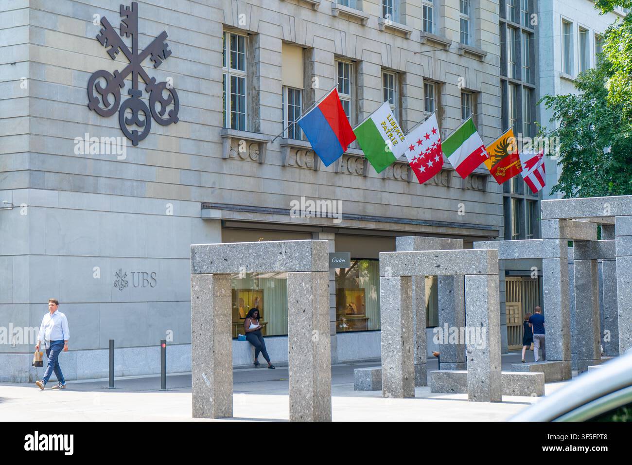 UBS-Schild an der Straßenwand des UBS-Bürogebäudes mit Flaggen am Eingang. AG Schweizerisches globales Finanzdienstleistungsunternehmen. UBS-Bank-Hauptsitz mit Flagge des Schweizer Kantons. Zürich, Schweiz – 23. Juni 2026 Stockfoto