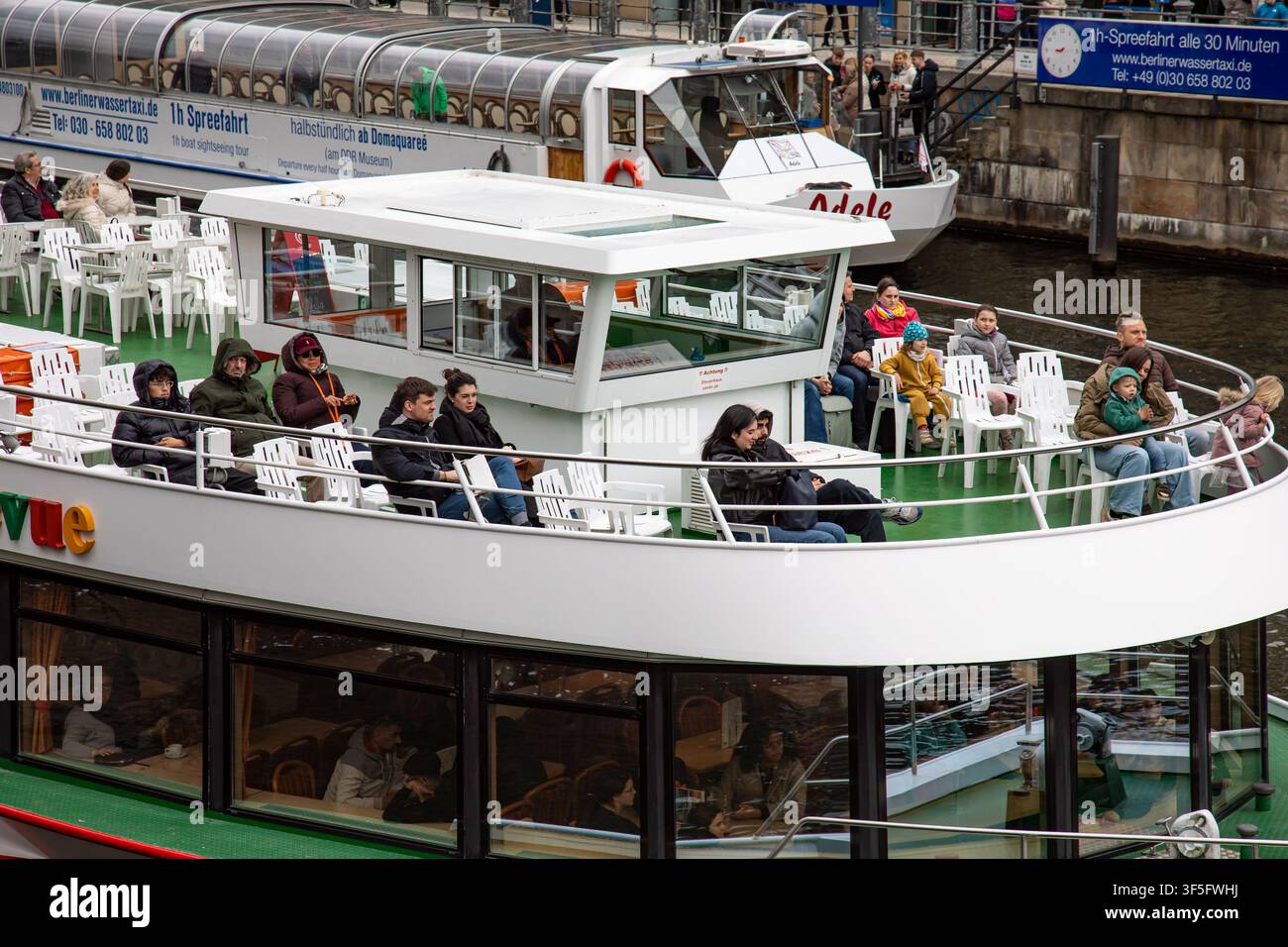 Touristen auf dem Oberdeck eines Flusskreuzfahrtschiffes oder Ausflugsschiffes an einem kalten Wintertag in Berlin, Deutschland Stockfoto