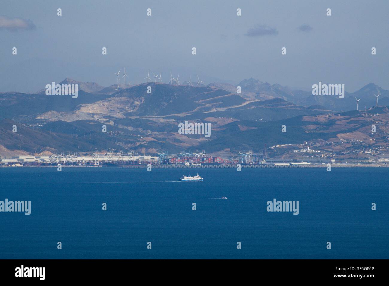 10.07.2026  Tanger Med Containerhafen an der marokkanischen Küste, gesehen über die Straße von Gibraltar von Südspanien aus, mit Fähre, Windrädern und Stockfoto